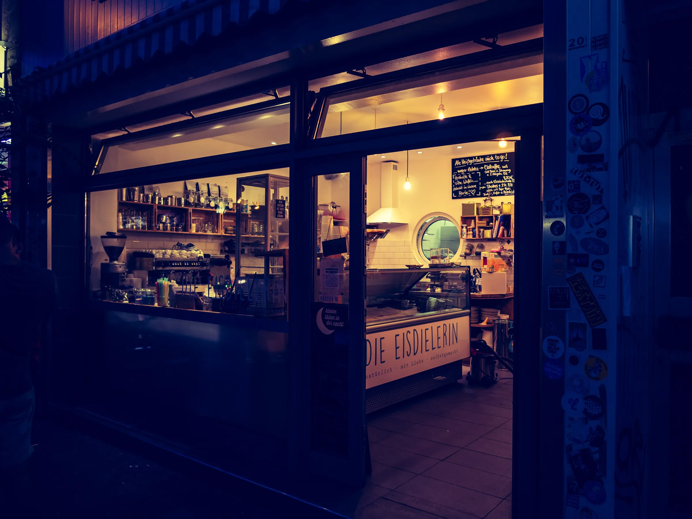 Warmly lit cafe interior at night with a sign reading "Die Eisdiele".