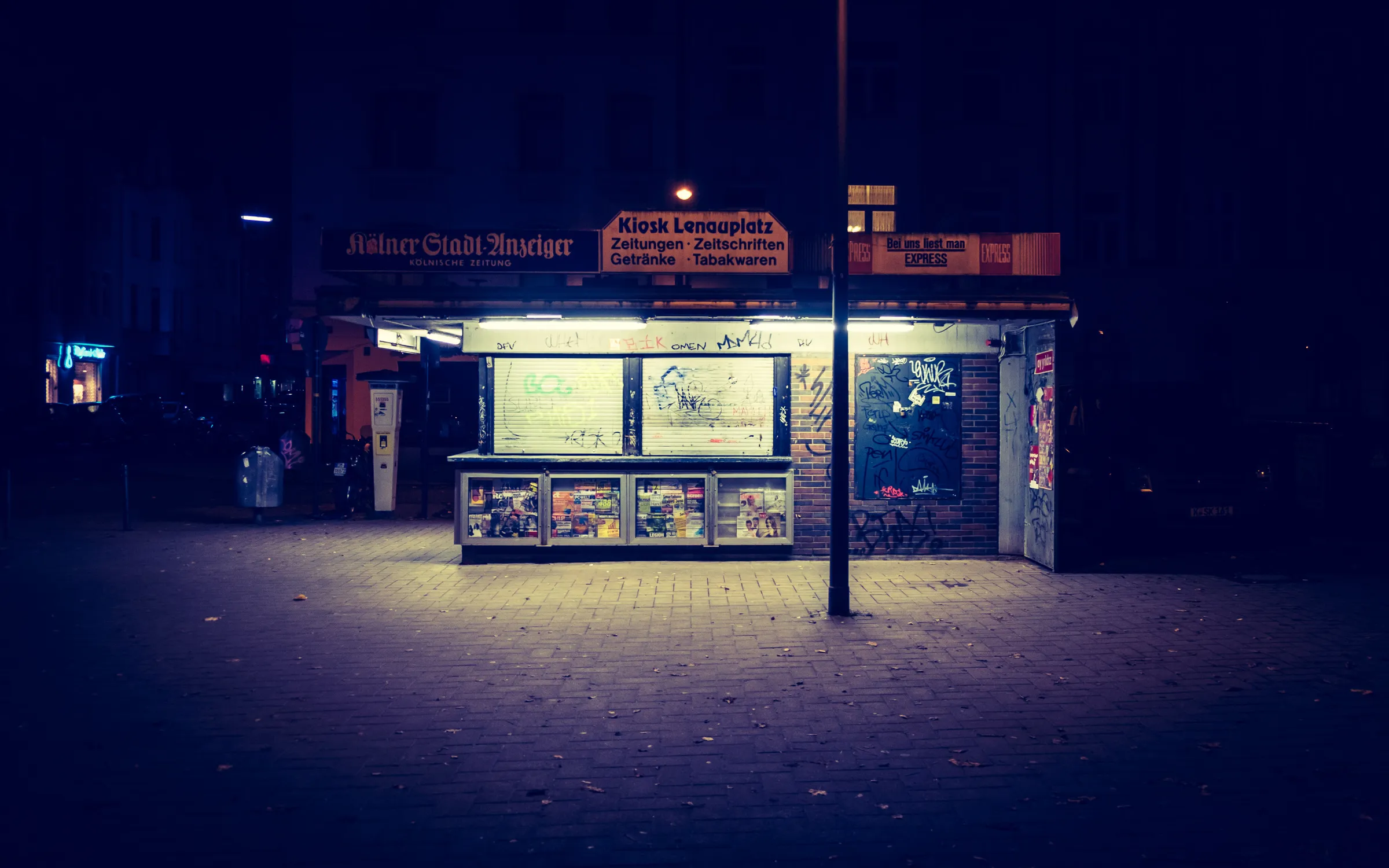 Night scene at a street food stand, warmly lit against dark surroundings, displaying posters and signs.