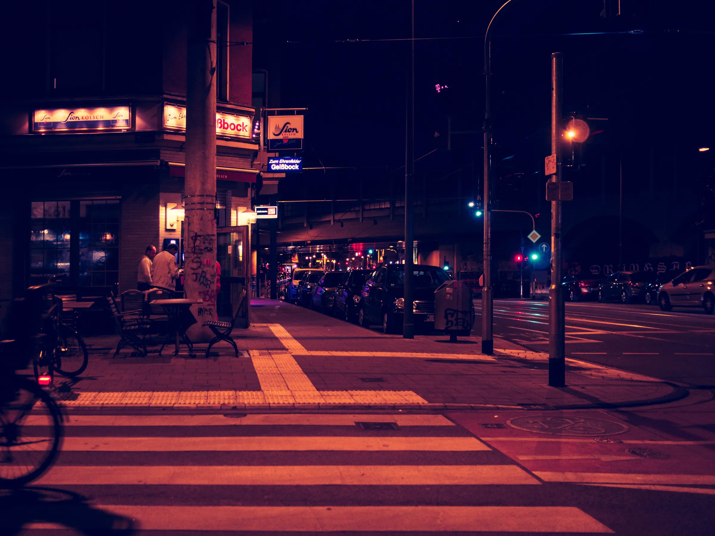 Pedestrians on quiet street at night, illuminated by shop lights and street lamps.