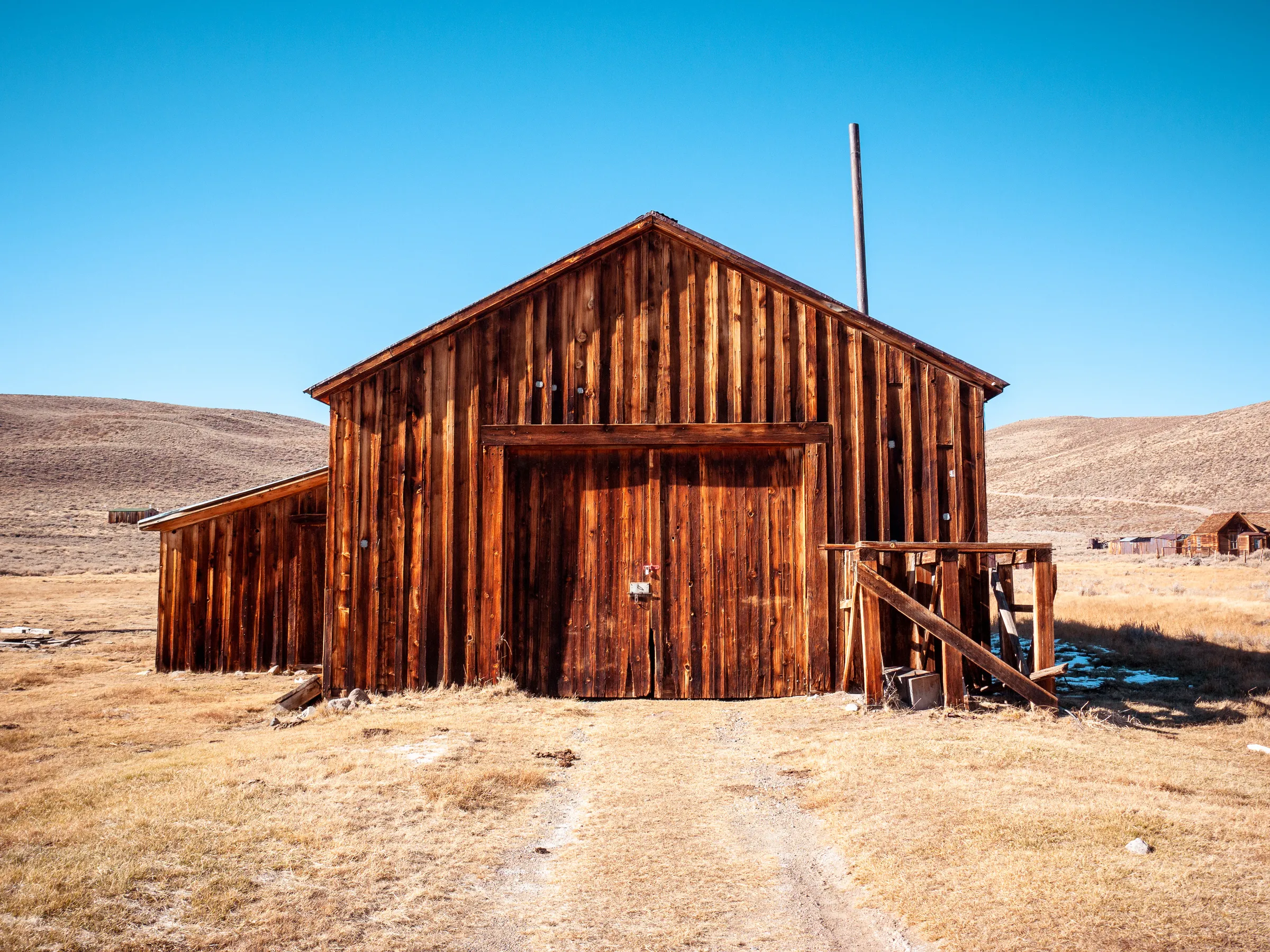 Weathered wooden barn with double doors, set in a dry, hilly landscape under clear blue sky.