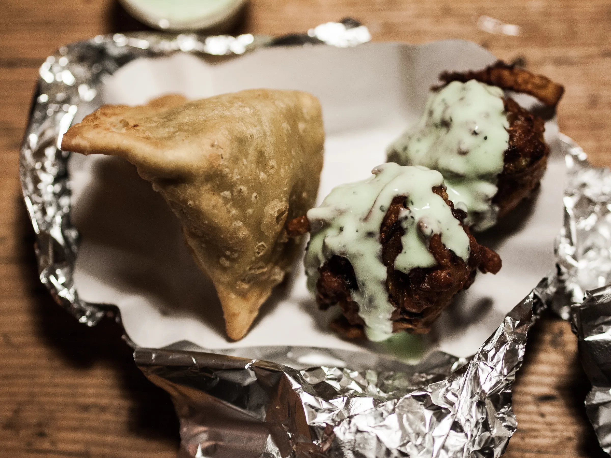Fried pastry triangle with crinkled edges next to a meatball in creamy sauce on tinfoil.