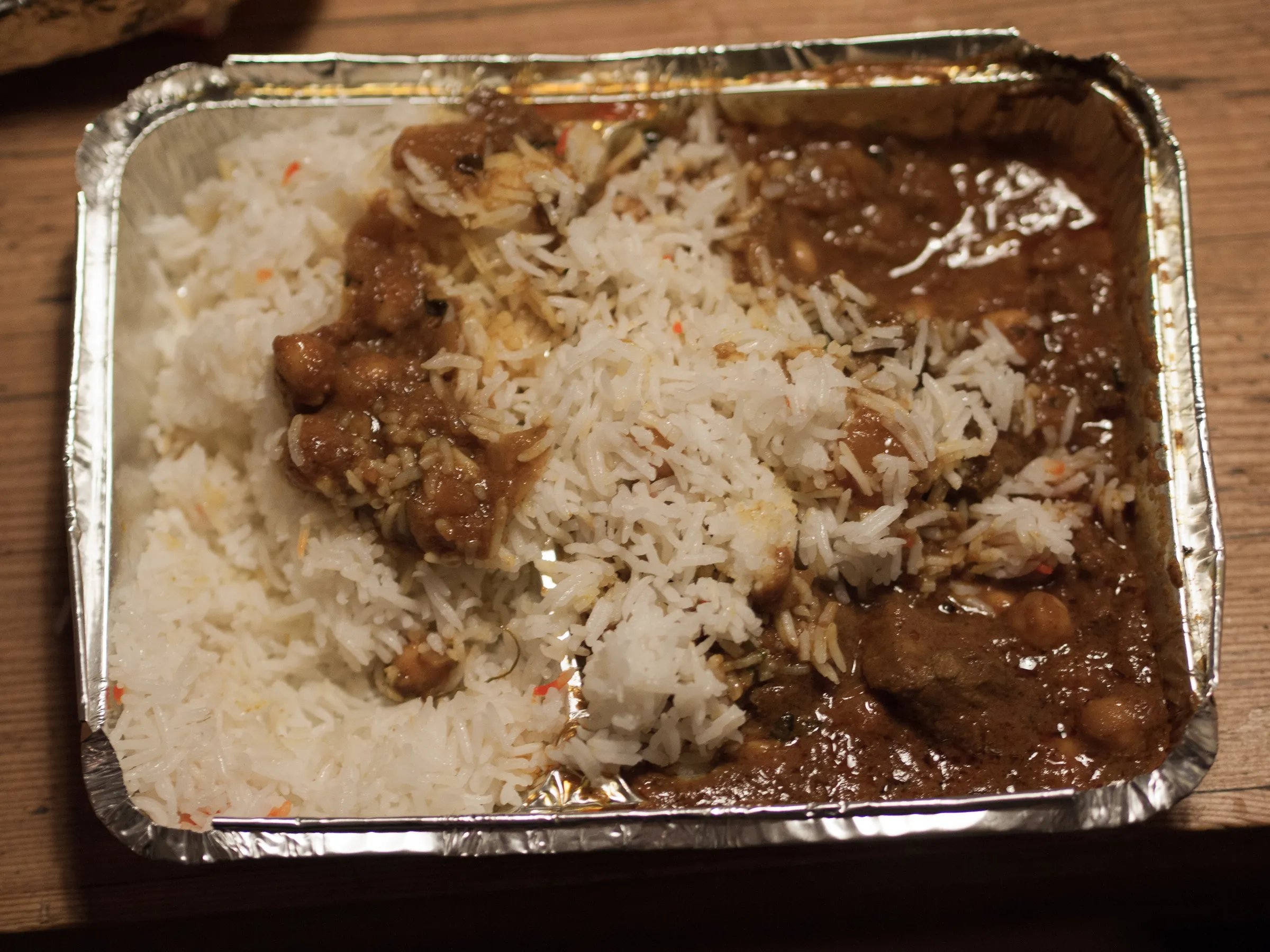 Tin tray with white rice and dark curry, wooden table background.