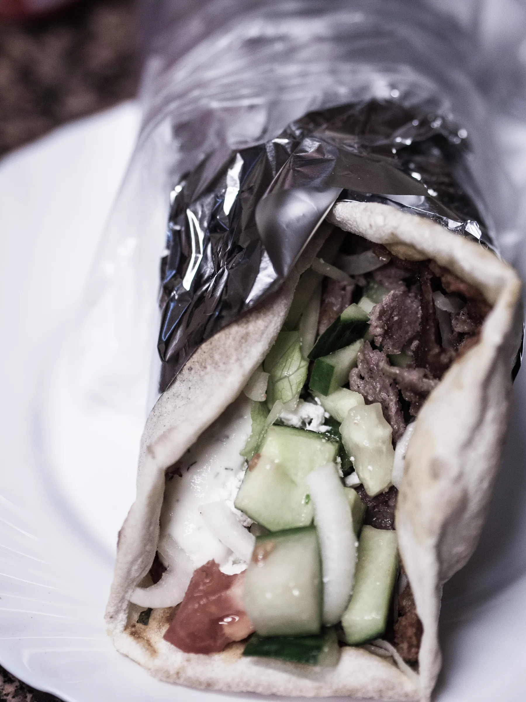 Wrapped sandwich with meat, cucumber, and tomato on a plate.