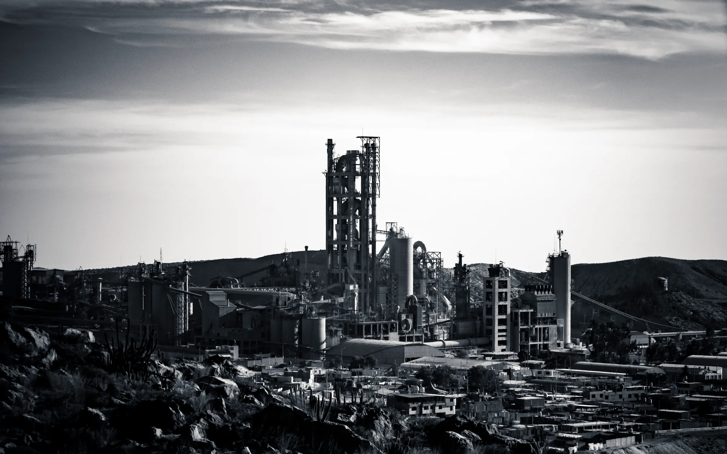 Industrial complex with towering structures, set against a hillside, captured in black and white.
