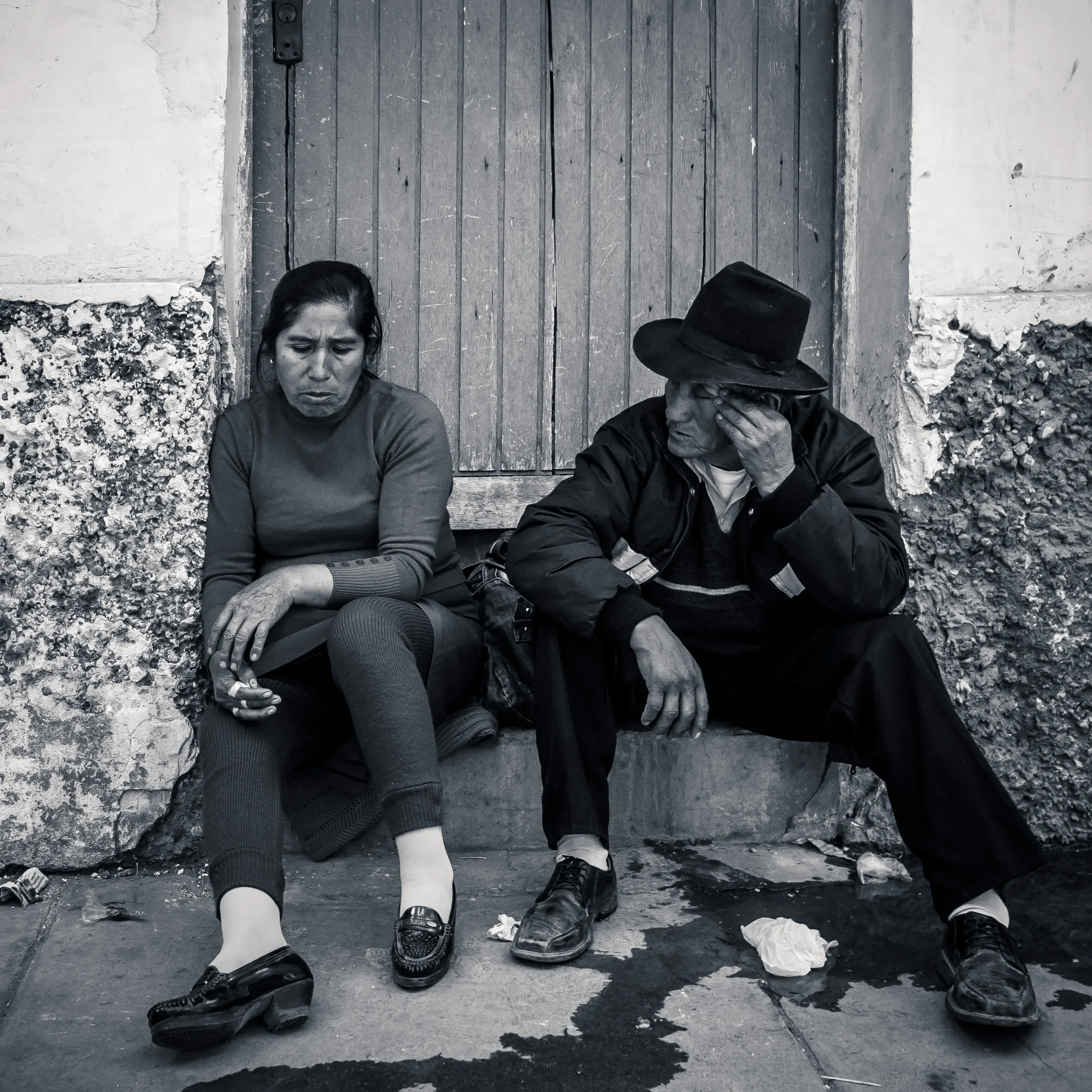 Two people sitting outside a wooden door, one resting her head on her hand, the other with his face covered.