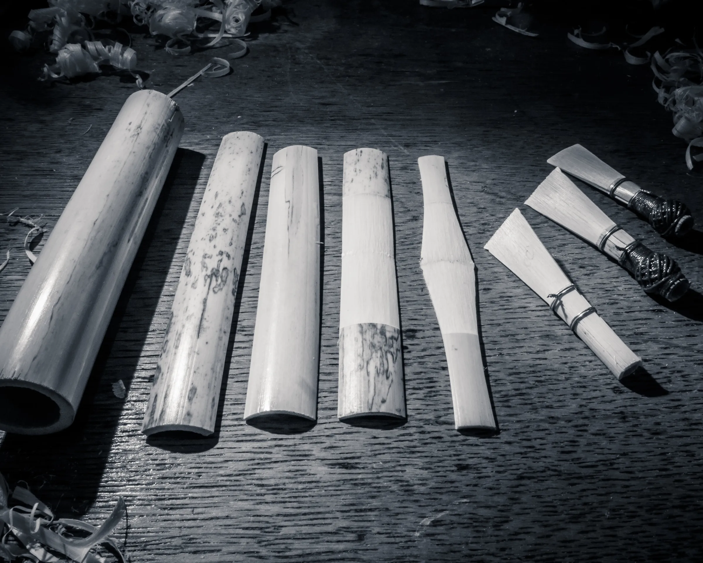 Five bamboo sticks in various stages of being hollowed out on a workbench, with tools nearby.