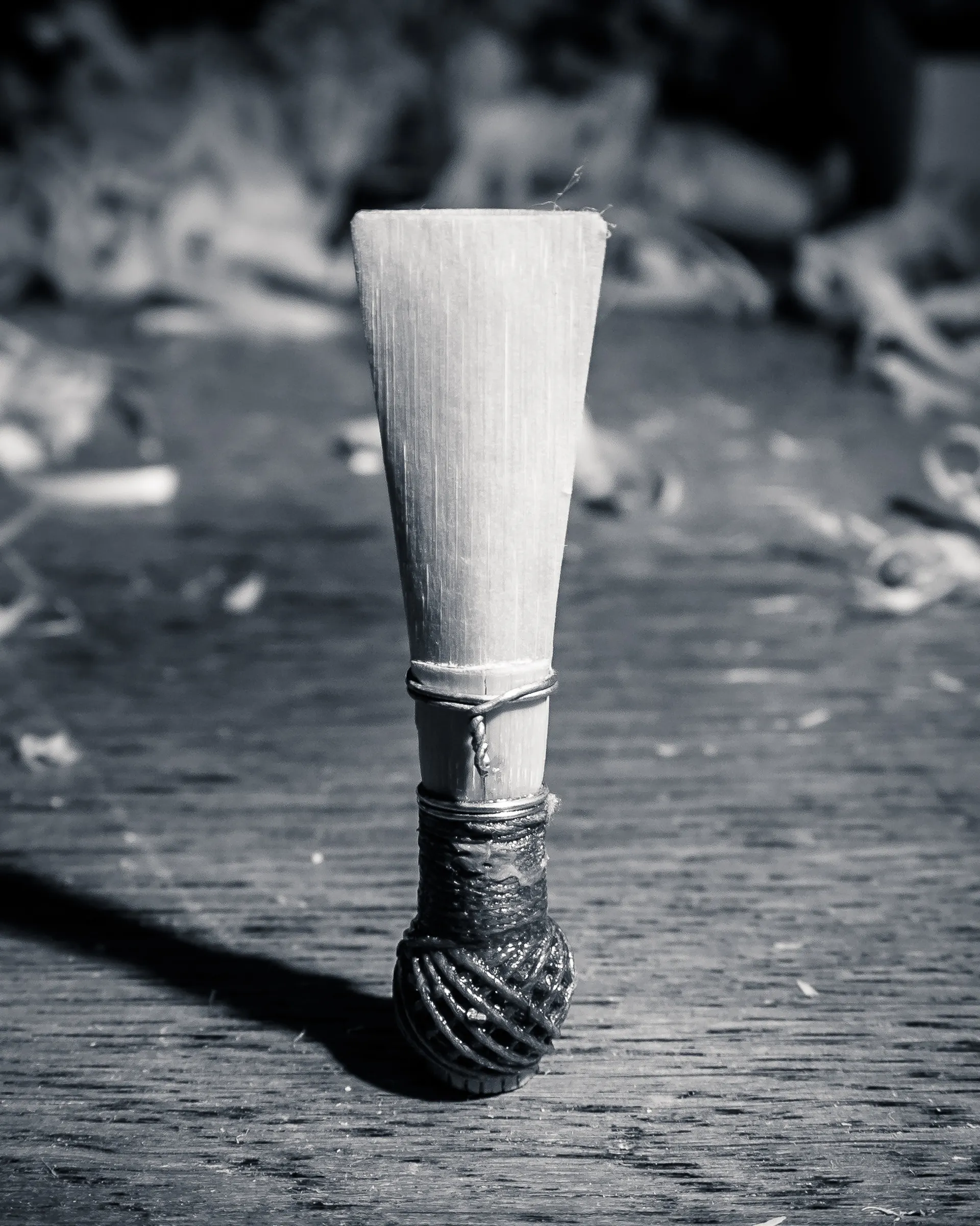 Bamboo stick with wrapped end, standing on weathered wooden surface.