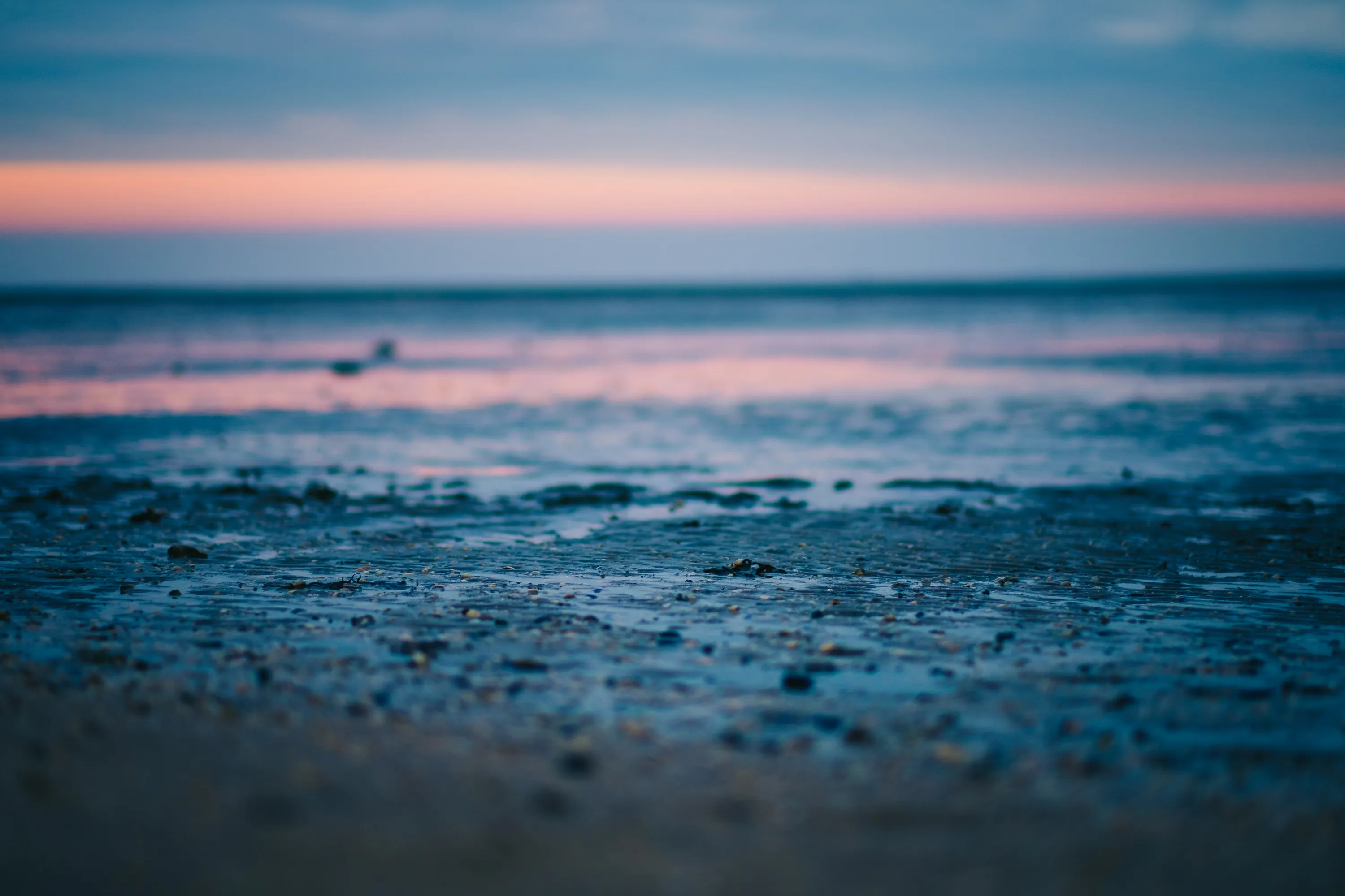 Beach at sunset with blurred horizon, pebbles in foreground.