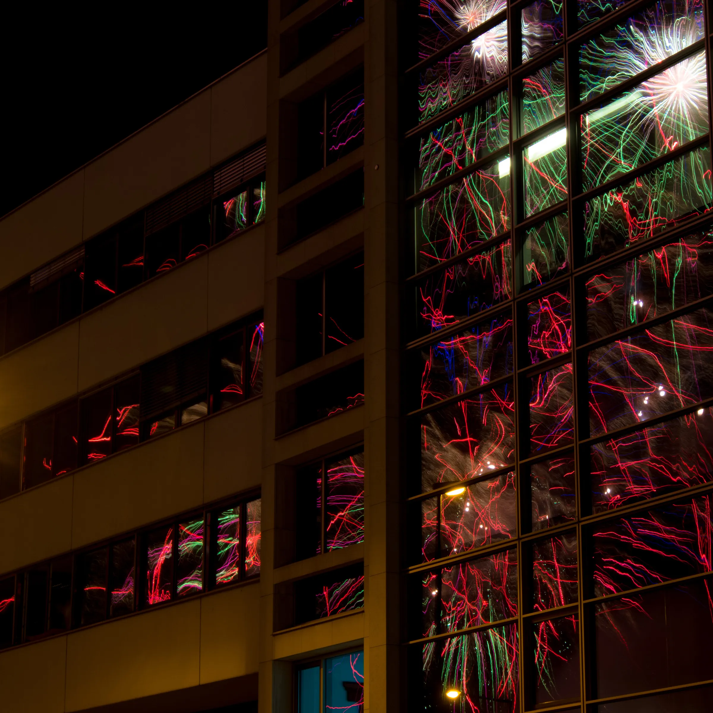 High-rise building at night with colorful fireworks reflections on its windows.