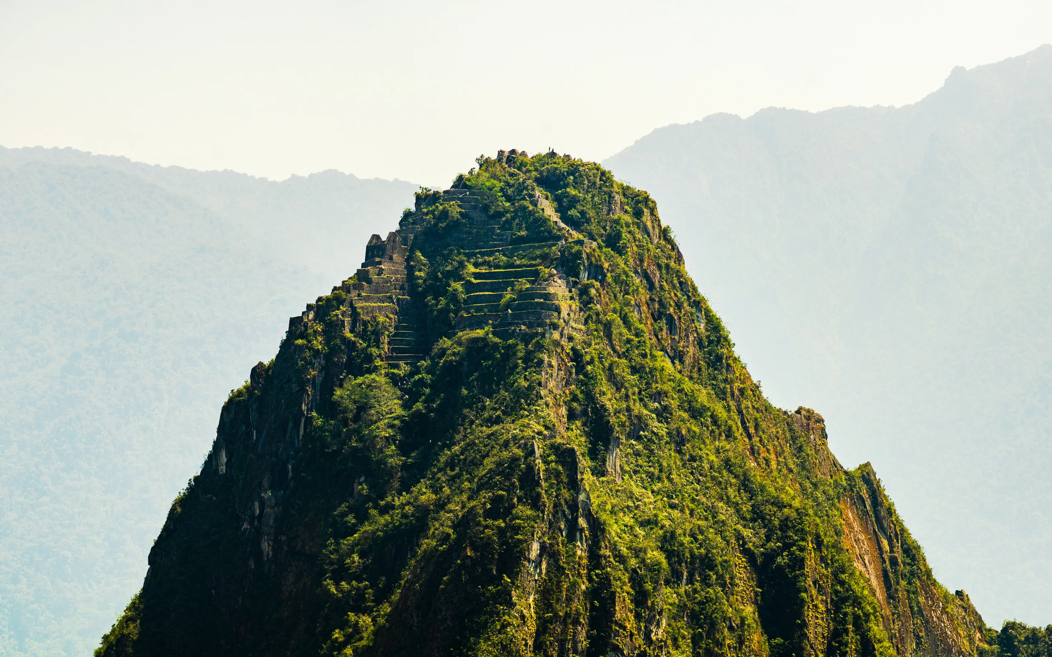 A green mountain with terraced steps, set against hazy mountains in the background.