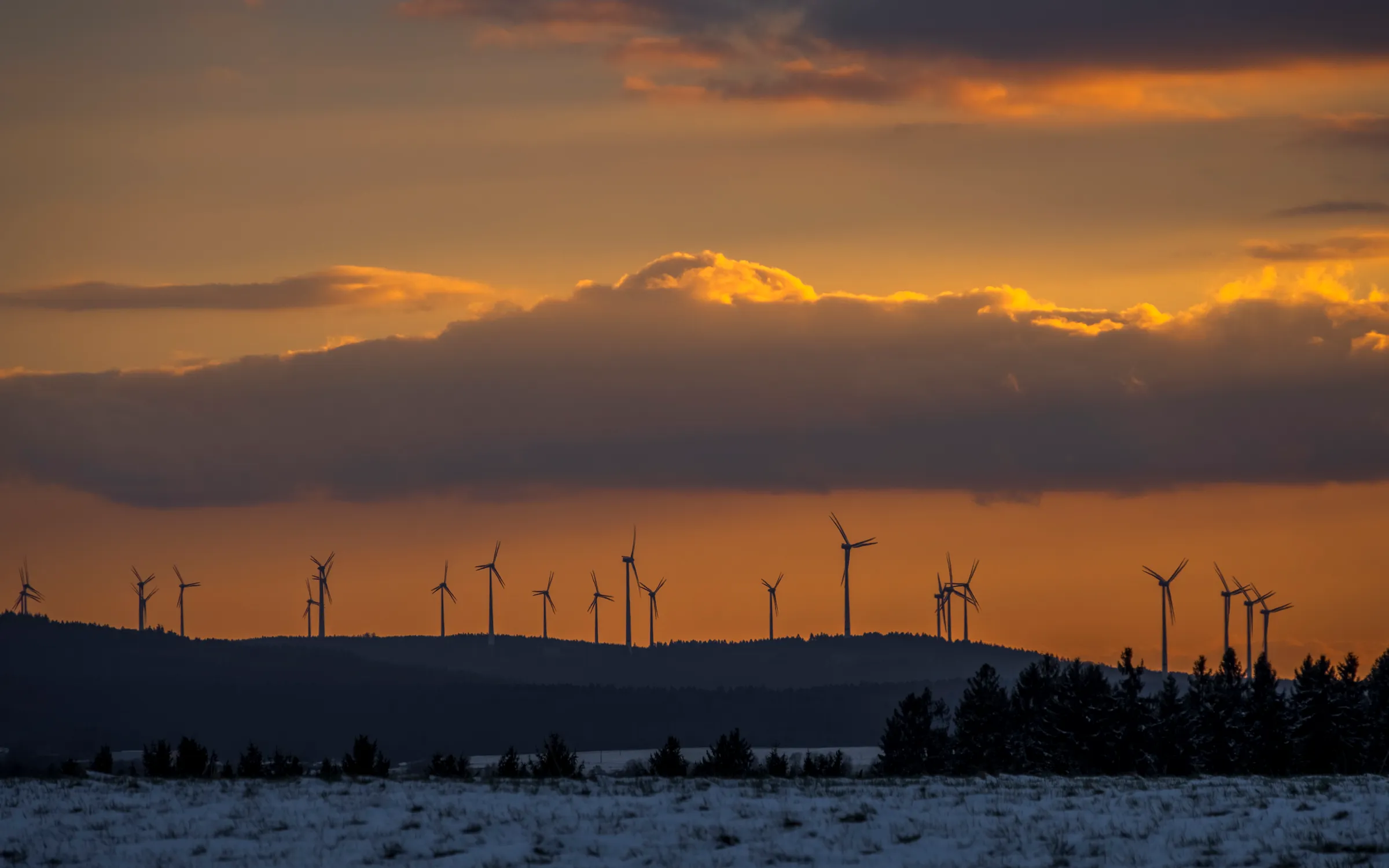 Sunset with wind turbines silhouetted against a colorful sky, snowy landscape.