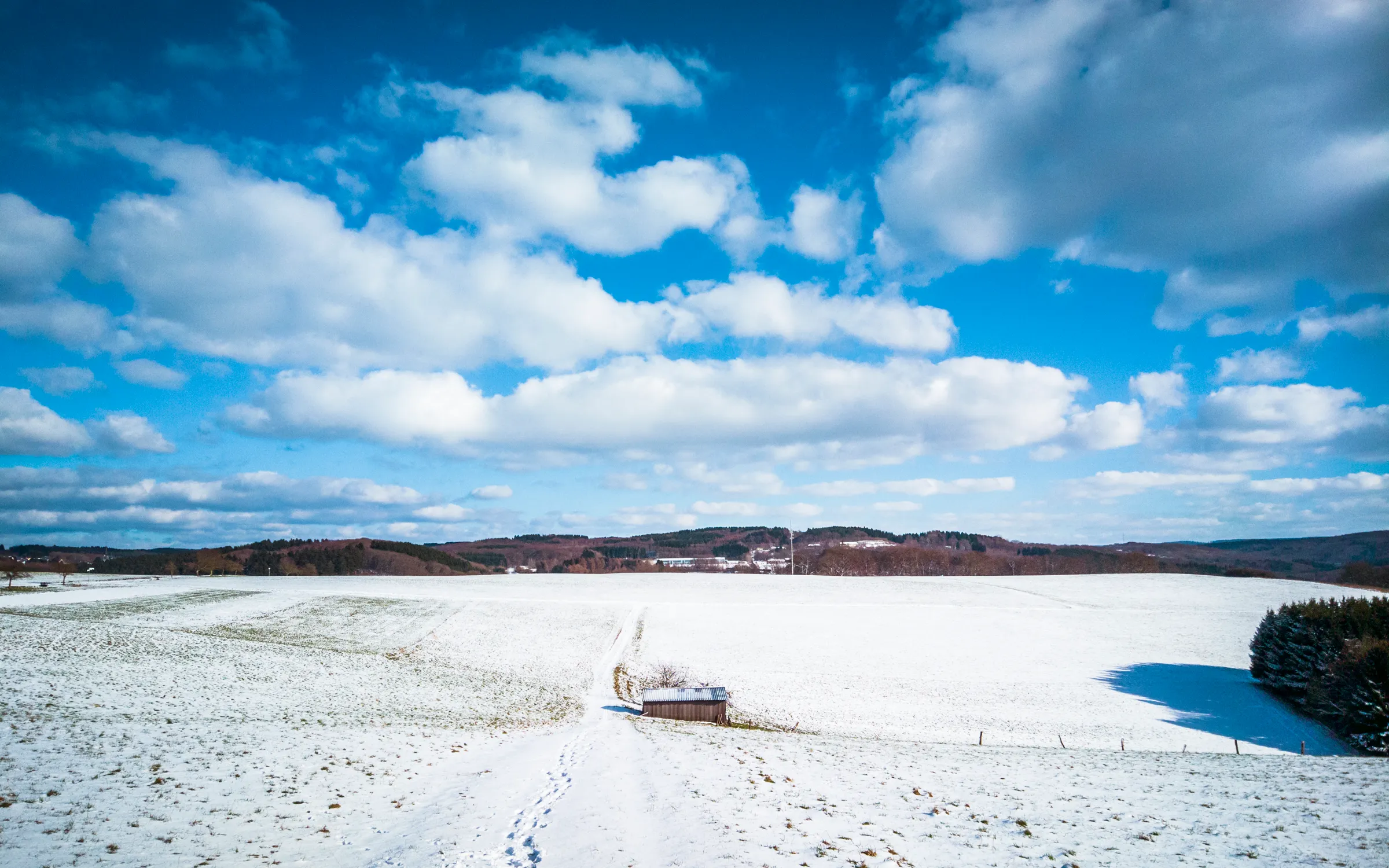 Snowy field with a solitary car on a road, under a blue sky with scattered clouds.