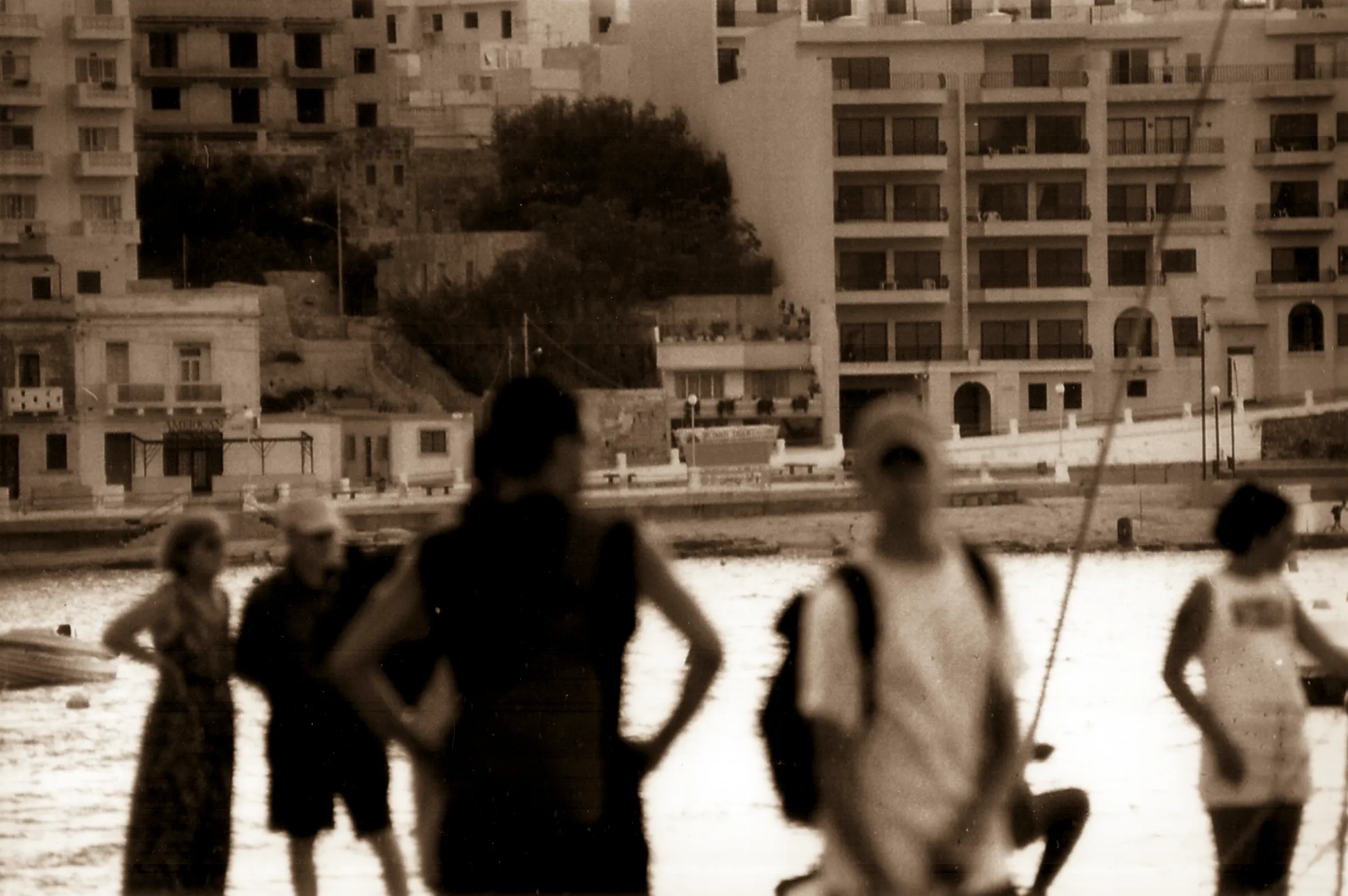 Four people wading in water with buildings in background.