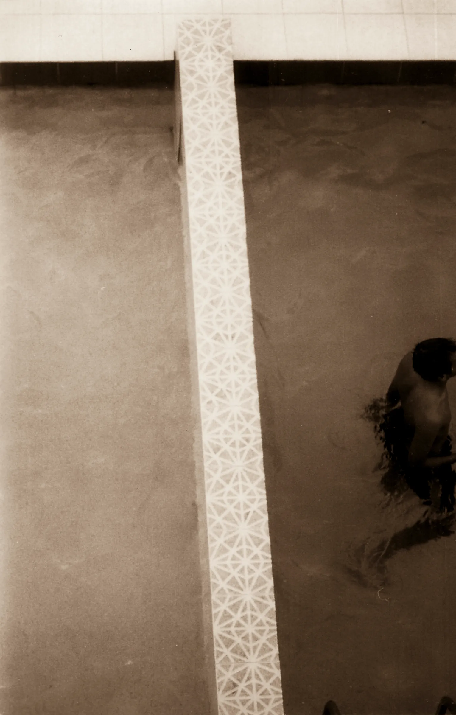 A person's reflection in a mirror next to a tiled wall.