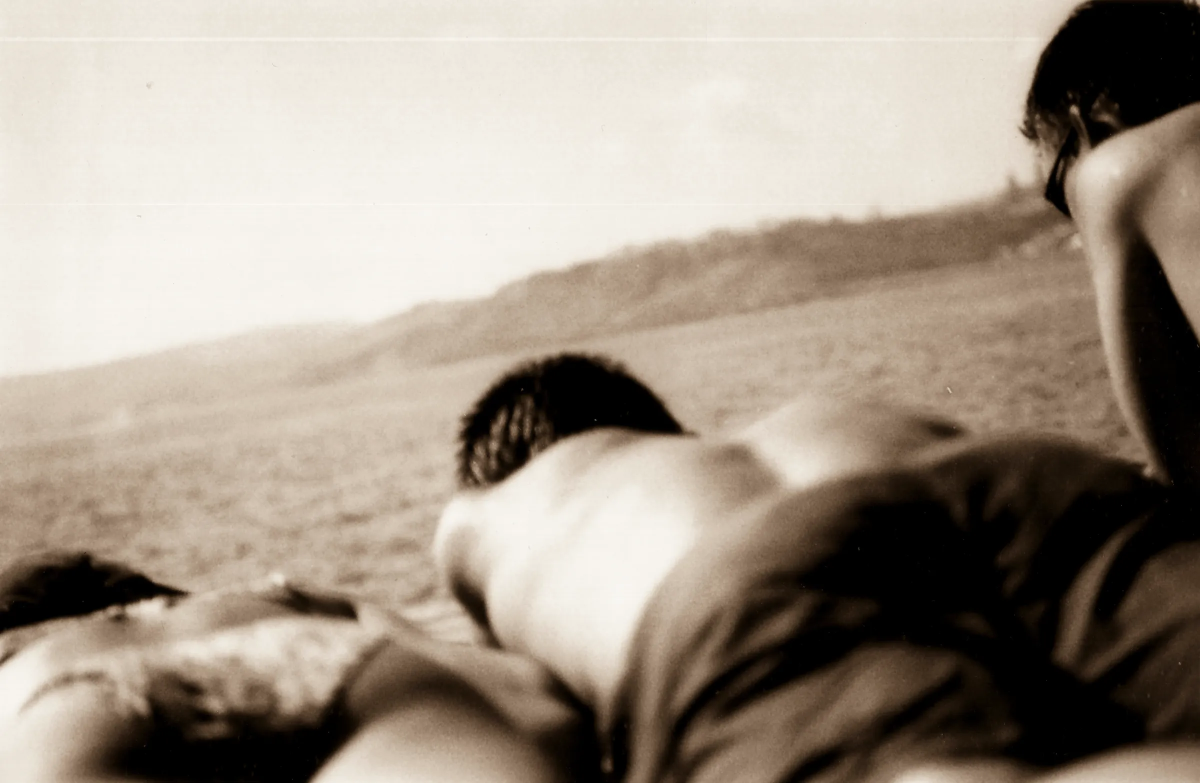 Couple lying on the ground, looking at a vast landscape with hills in the distance.