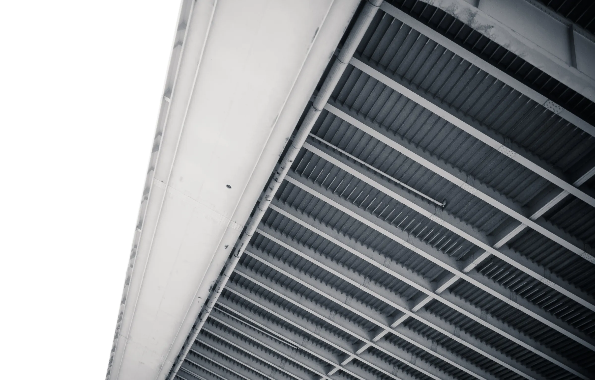 A close-up of a building's white exterior wall with vertical slats, viewed from below against a sky background.