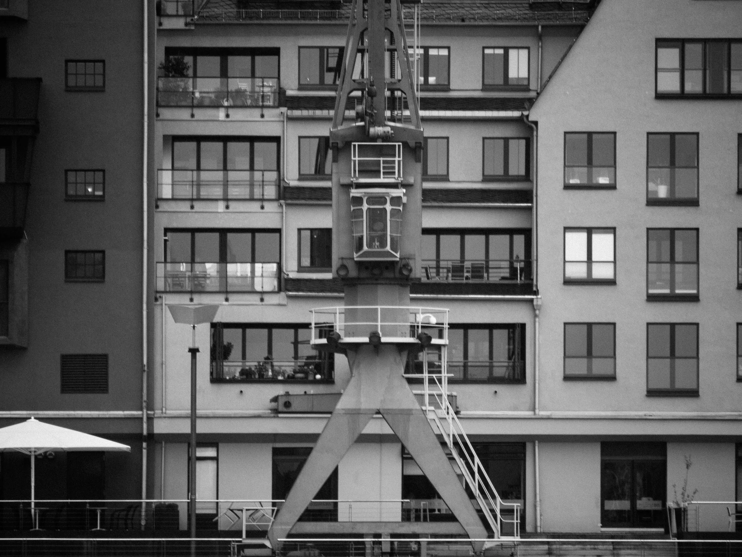 Crane in front of residential buildings with balconies and a car parked nearby.