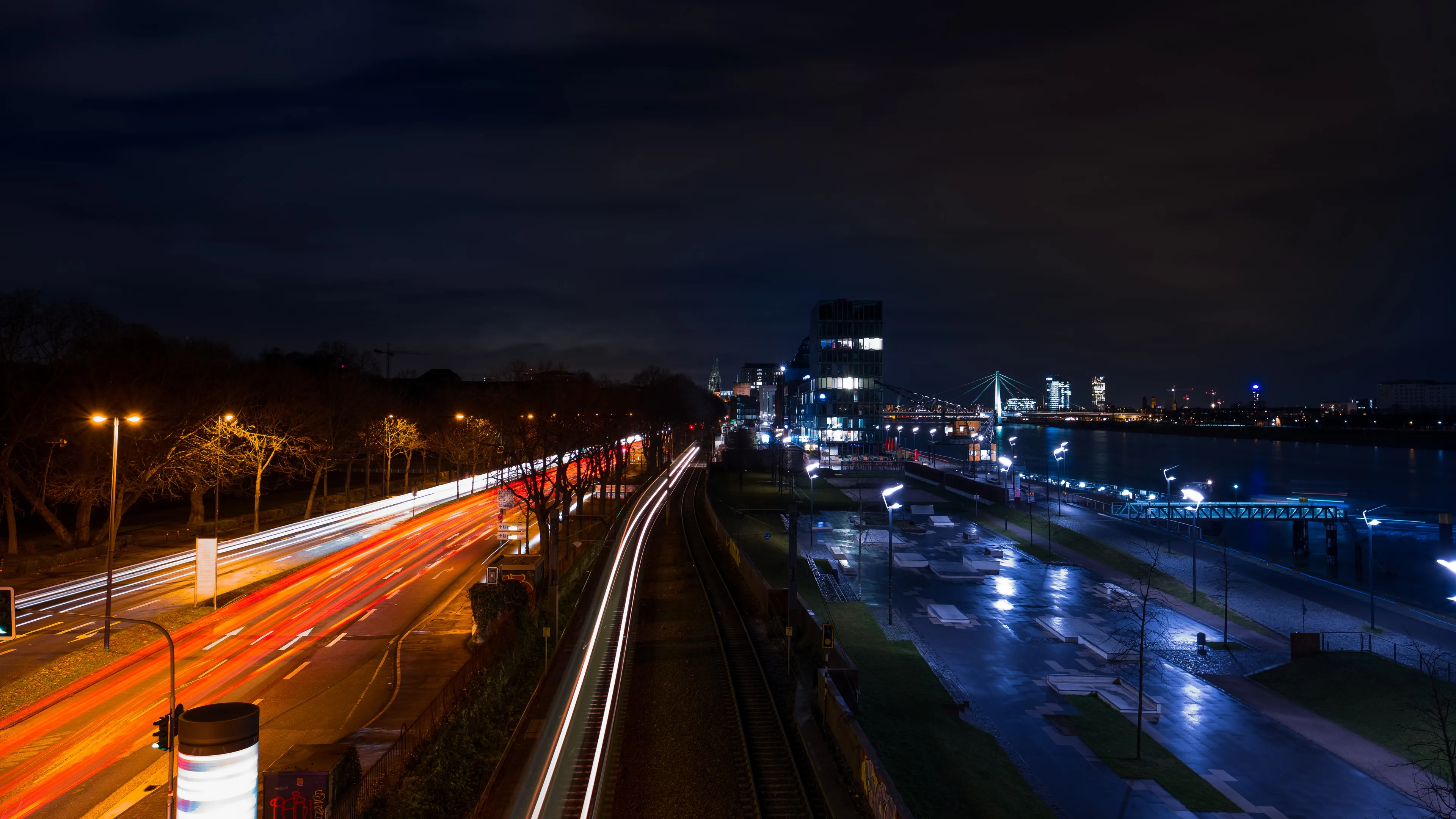 Night cityscape with highway, streaks of car lights, a river, and skyline buildings illuminated.