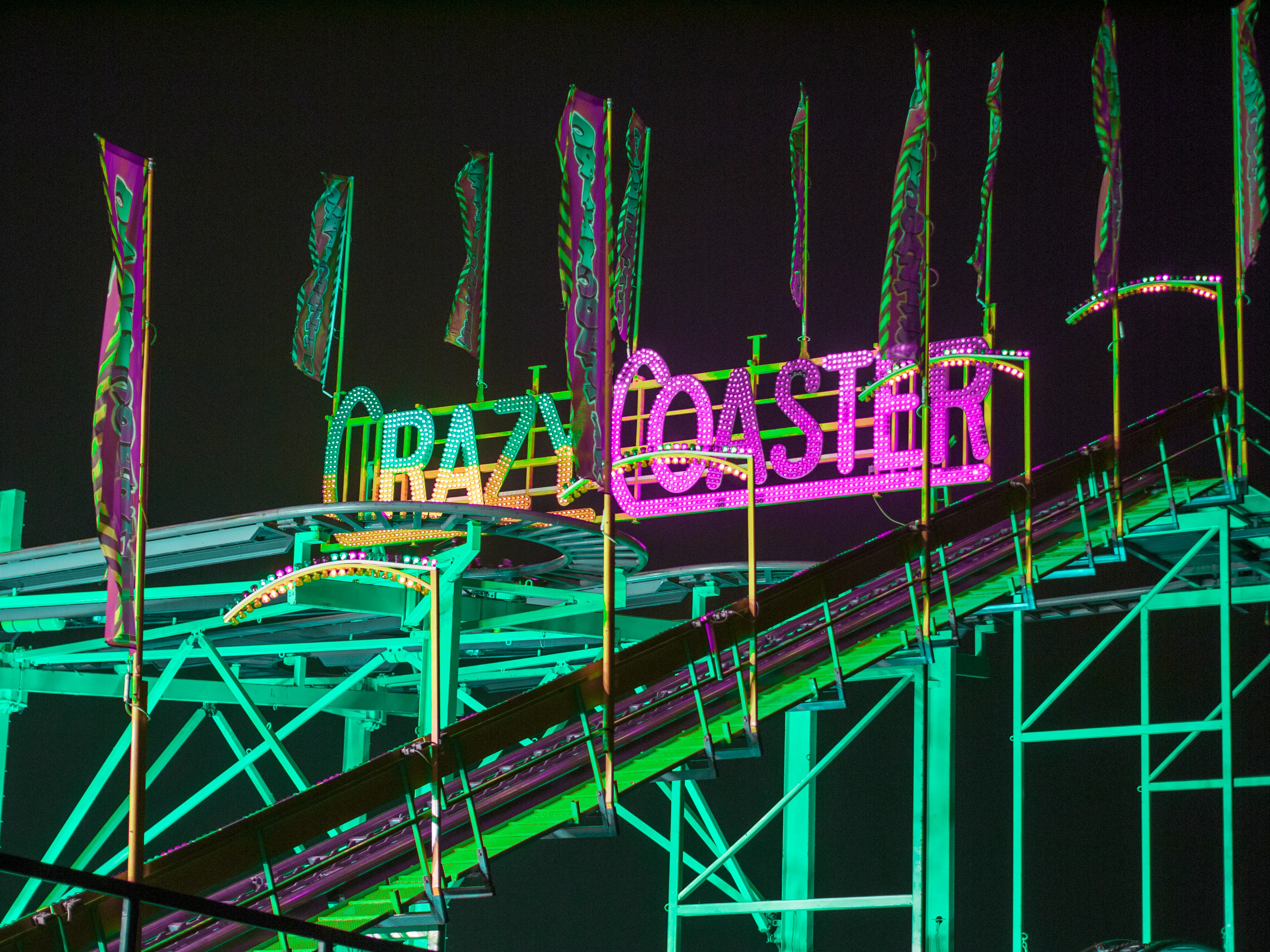 Neon signs on a roller coaster track at night.