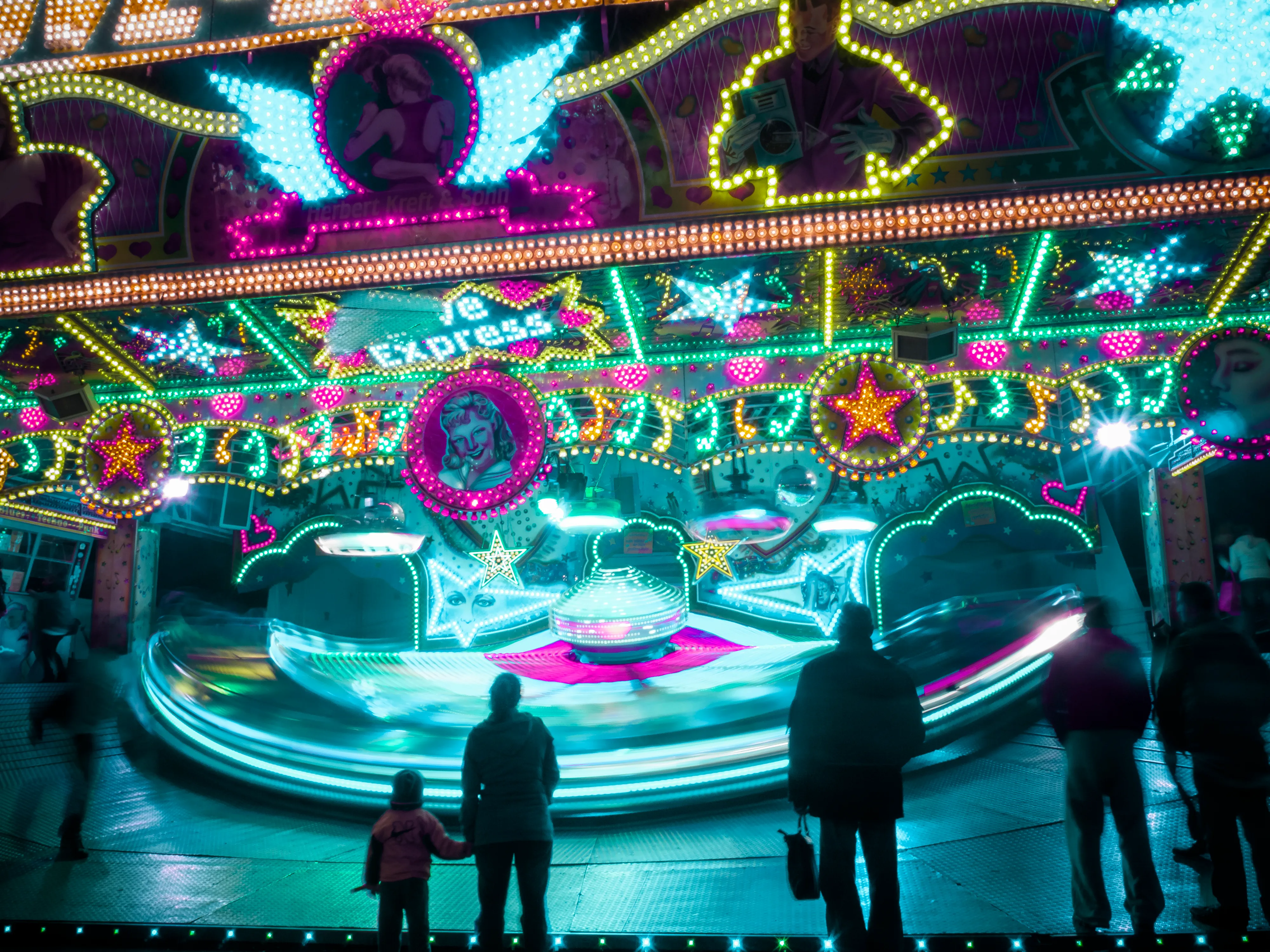 Colorful carousel at night with illuminated lights, a family watching, vibrant decorations.