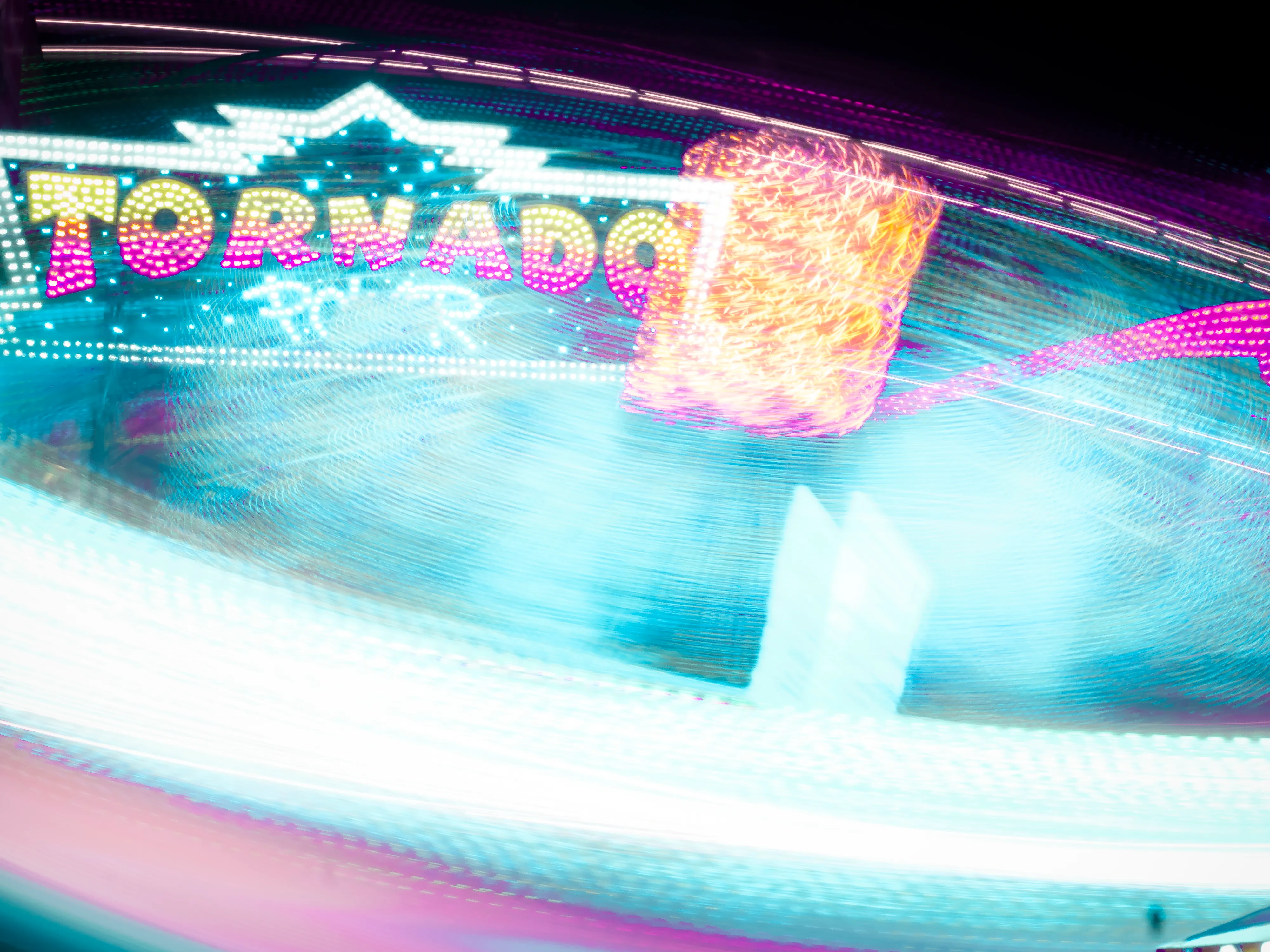 Brightly lit carnival ride, "Tornado", spinning at night with colorful streaks of light.