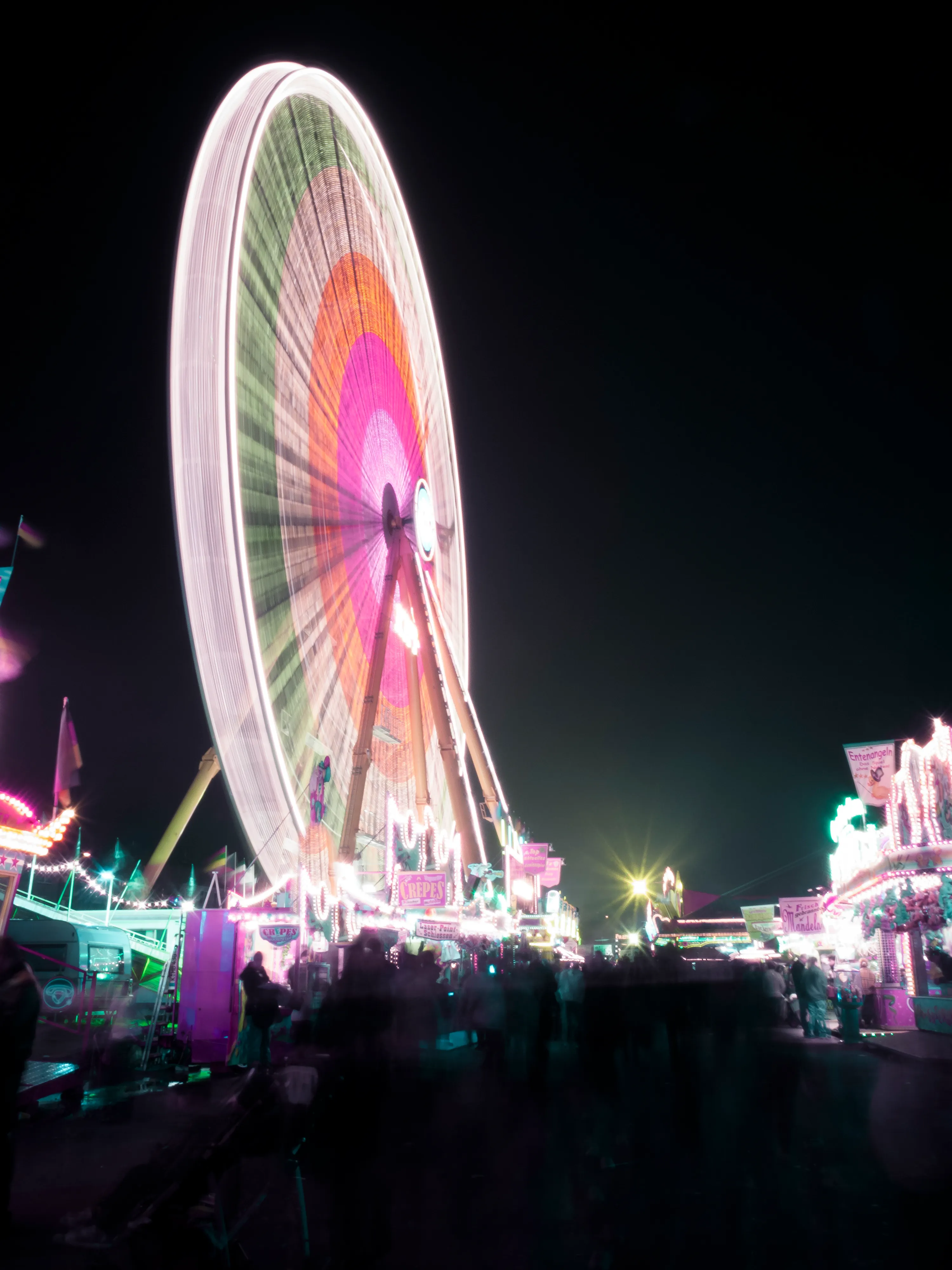Colorful Ferris wheel lit at night with a crowd below.