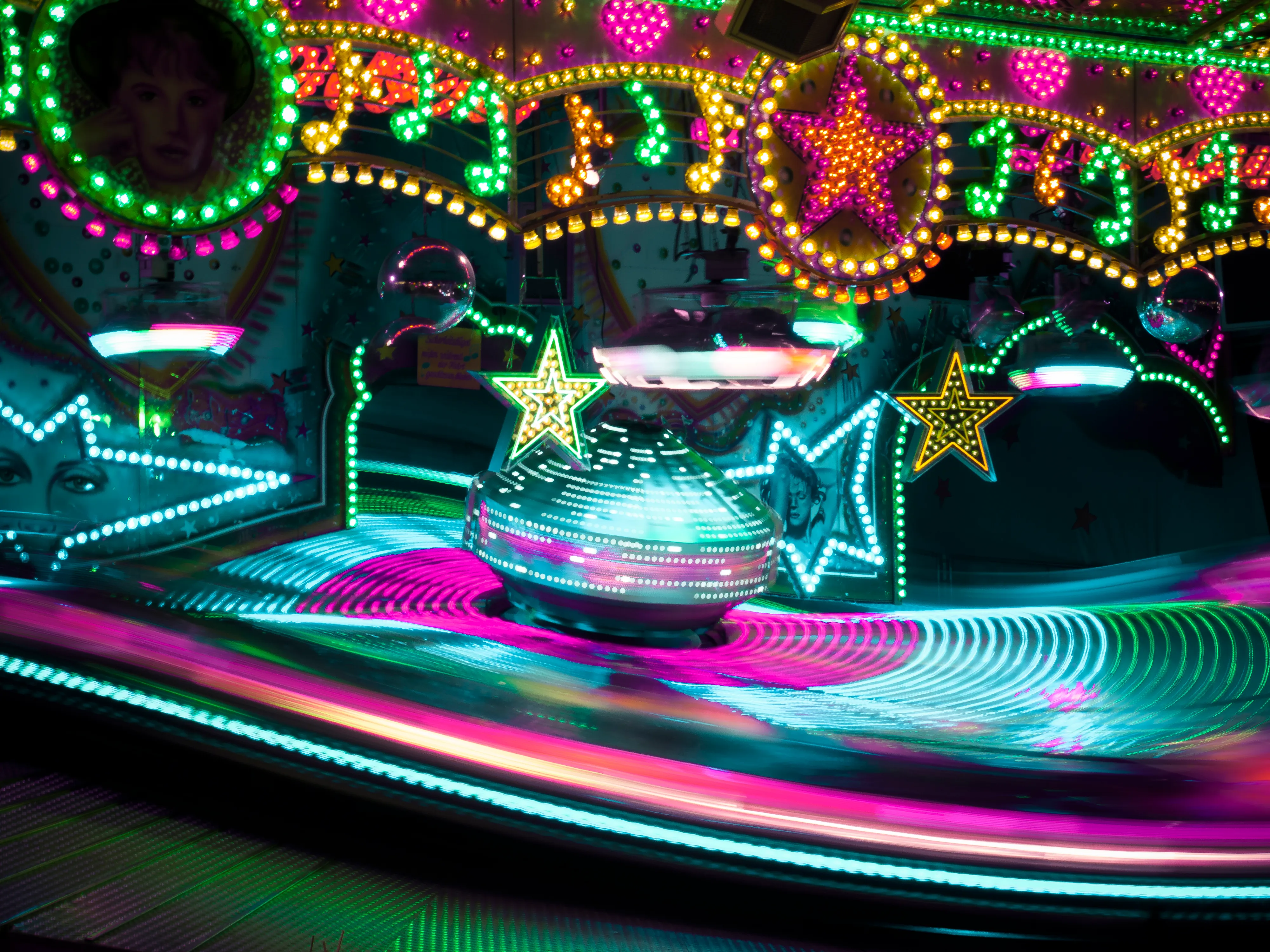 Colorful spinning carnival ride with bright neon lights, stars, and circular patterns at night.