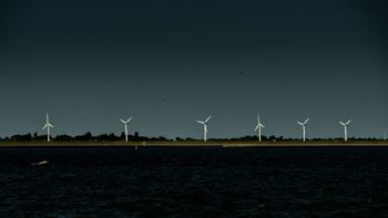 Five wind turbines on a dark, horizontal line against a starry night sky and calm water.