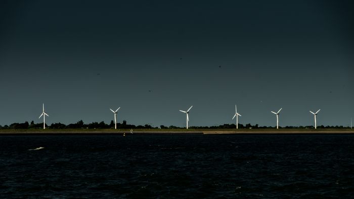Five wind turbines on a dark, horizontal line against a starry night sky and calm water.