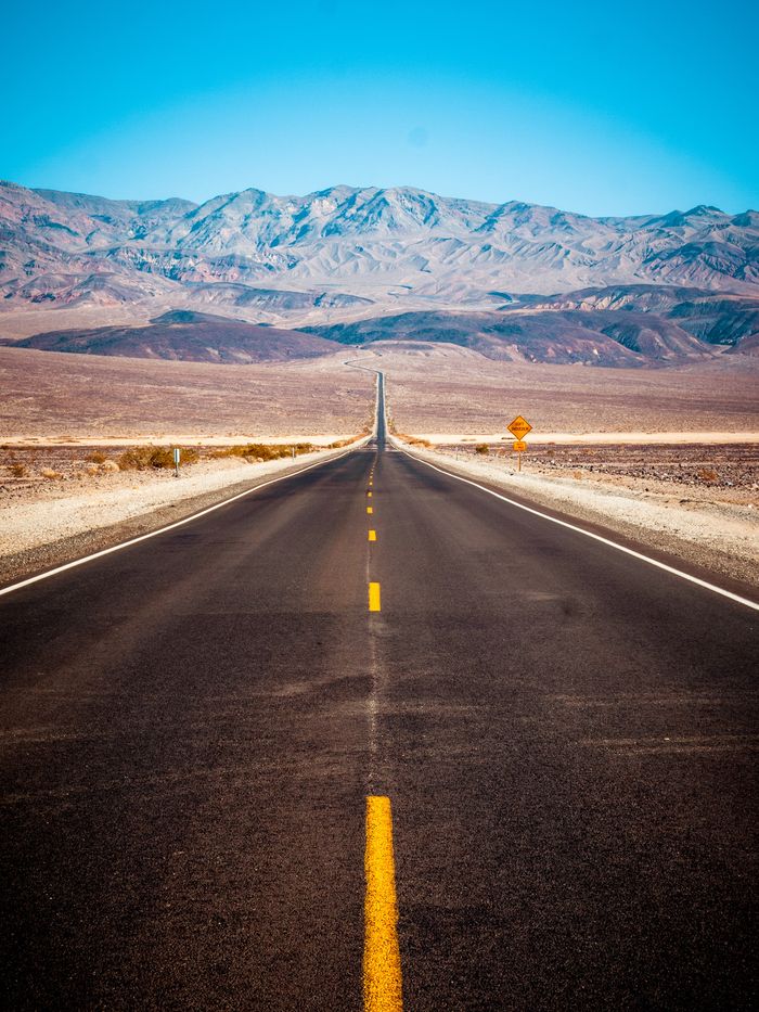 A long, straight road stretching towards mountains in a vast desert landscape.