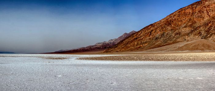 Desert landscape with salt flats and distant red mountains under a blue sky.