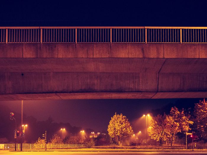 Concrete overpass lit by warm streetlights at night with trees below.