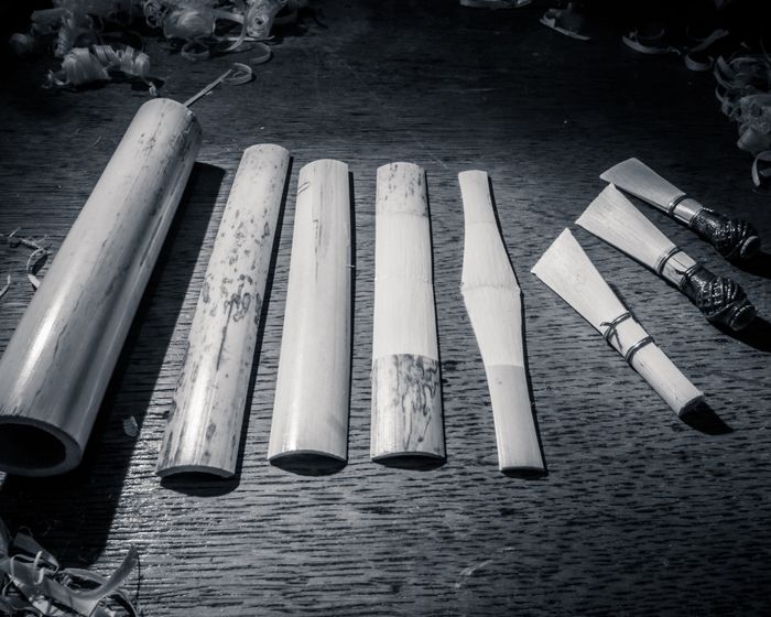 Five bamboo sticks in various stages of being hollowed out on a workbench, with tools nearby.