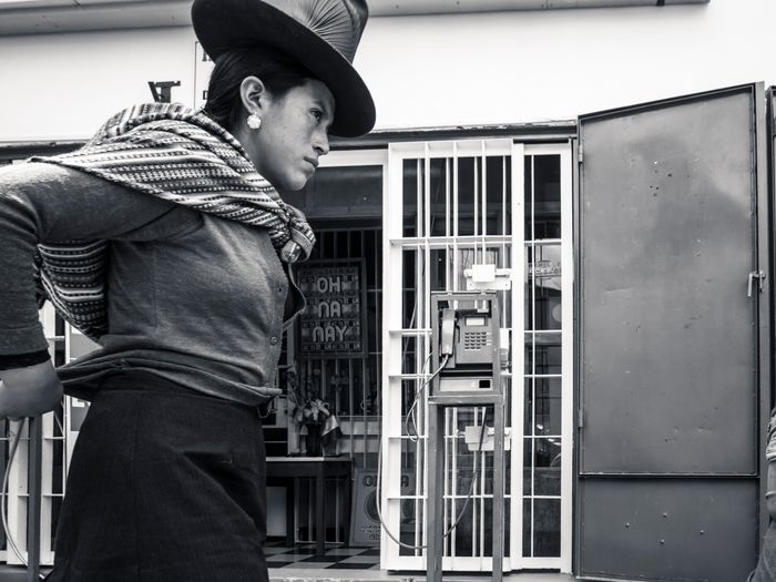 Person in traditional hat, scarf, looking away from a barred window with a telephone inside.