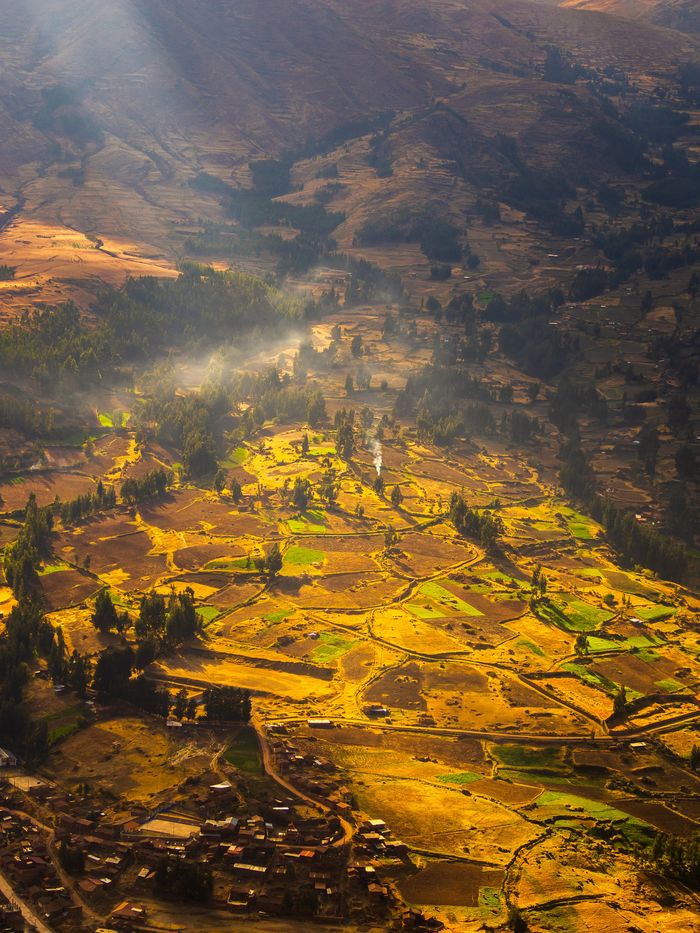 Aerial view of terraced fields in a valley, with morning mist and sunlight highlighting the landscape.