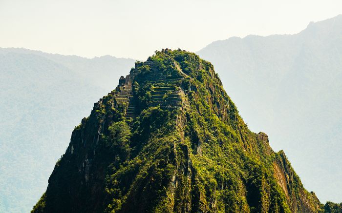 A green mountain with terraced steps, set against hazy mountains in the background.