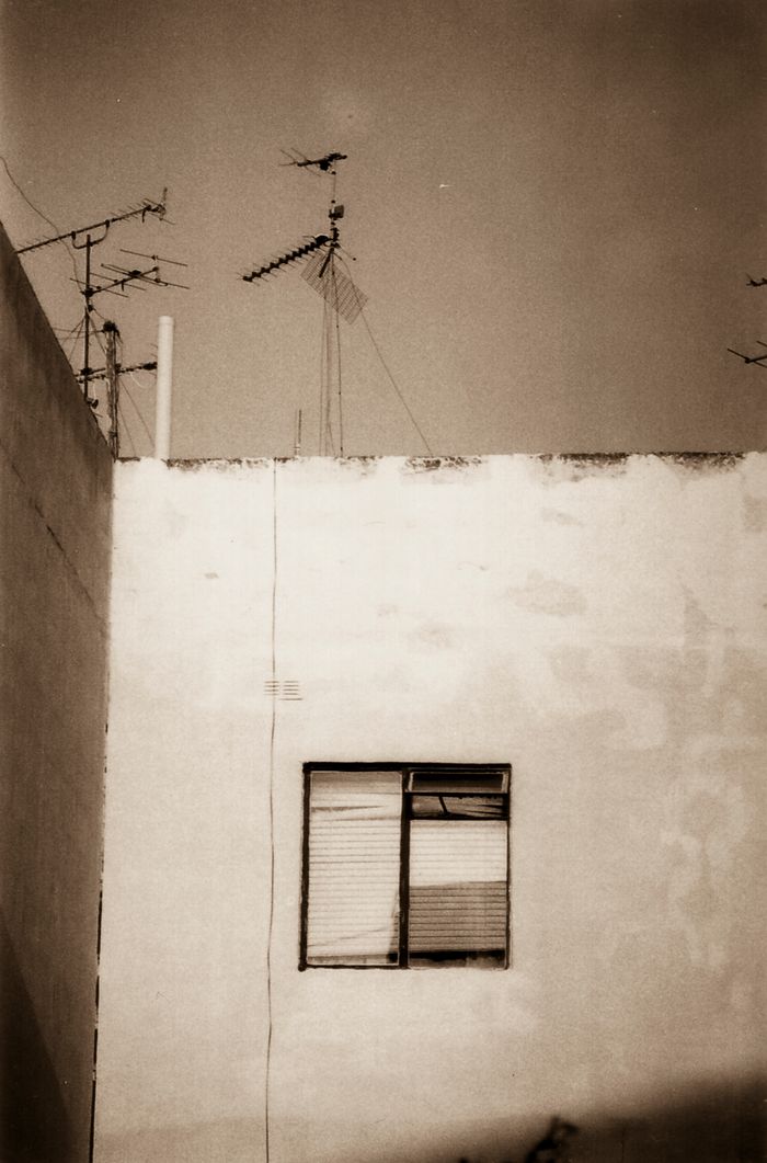 Building with two antennas on roof, single window below.