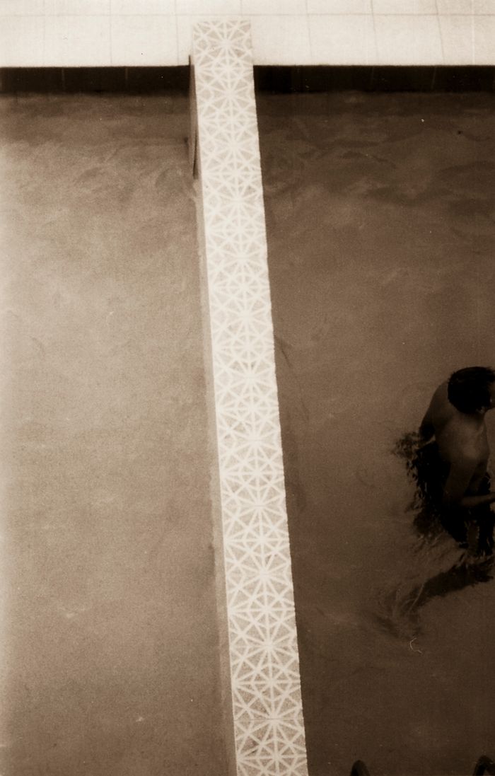 A person's reflection in a mirror next to a tiled wall.