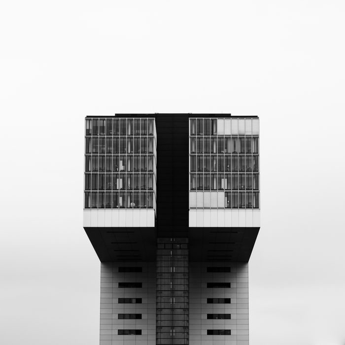 Tall building with two rectangular towers, connected by a horizontal section, against foggy sky.