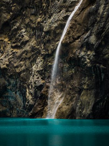Waterfall cascading down a rocky cliff into a vibrant turquoise pool, surrounded by rugged terrain.
