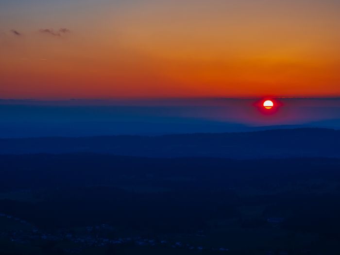 Sunset over hazy mountains, red sun partially obscured by mist.