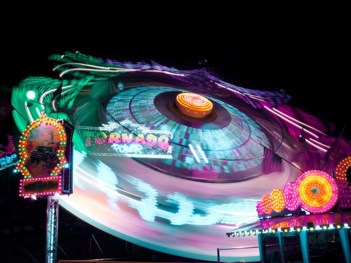 A vibrant carnival ride, Tornado, spinning at night with colorful lights, a dragon head at the top, and blurred motion from its rotation.