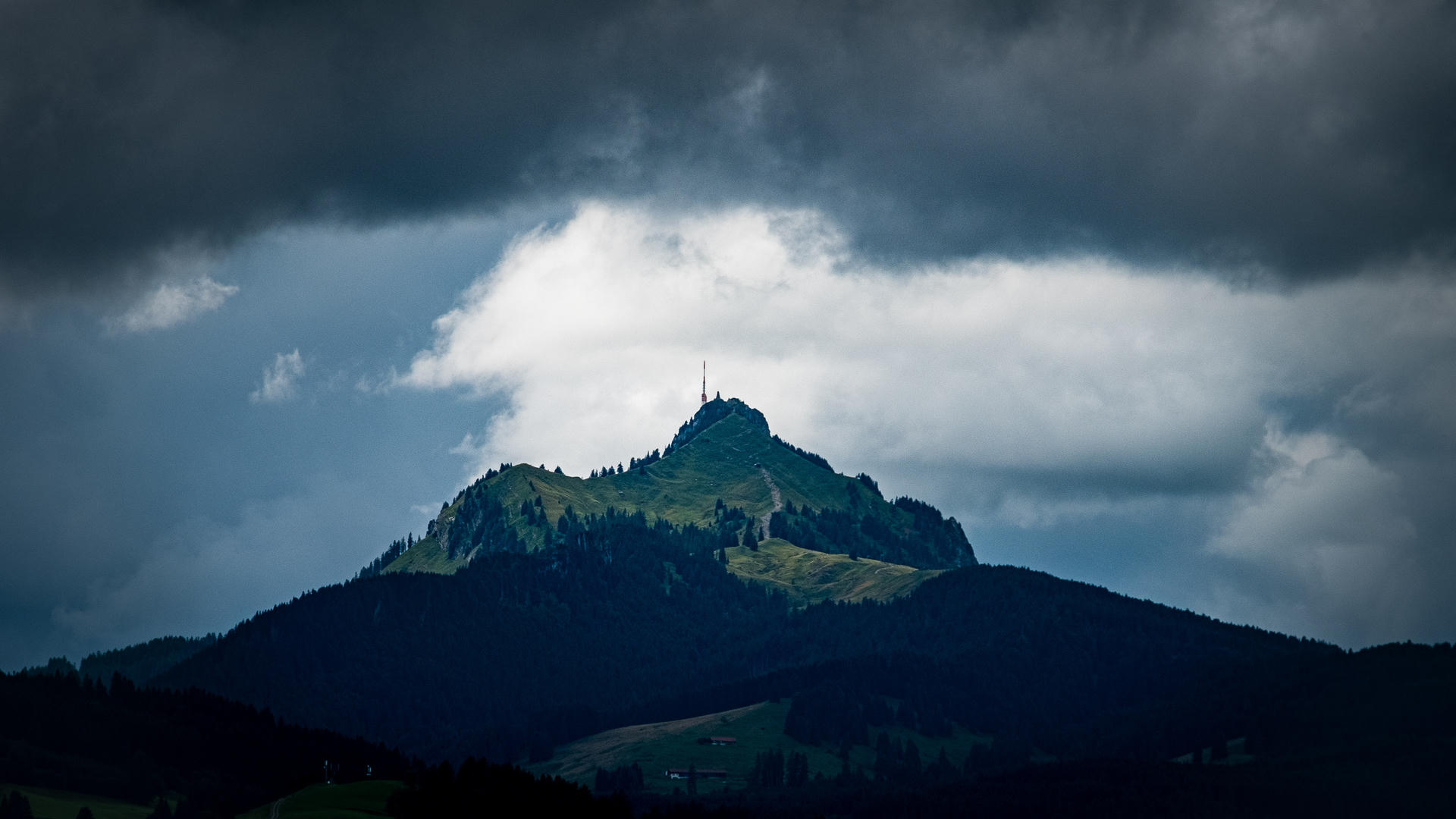 Mountain peak with a tower, dark clouds, dramatic lighting, silhouette of landscape.