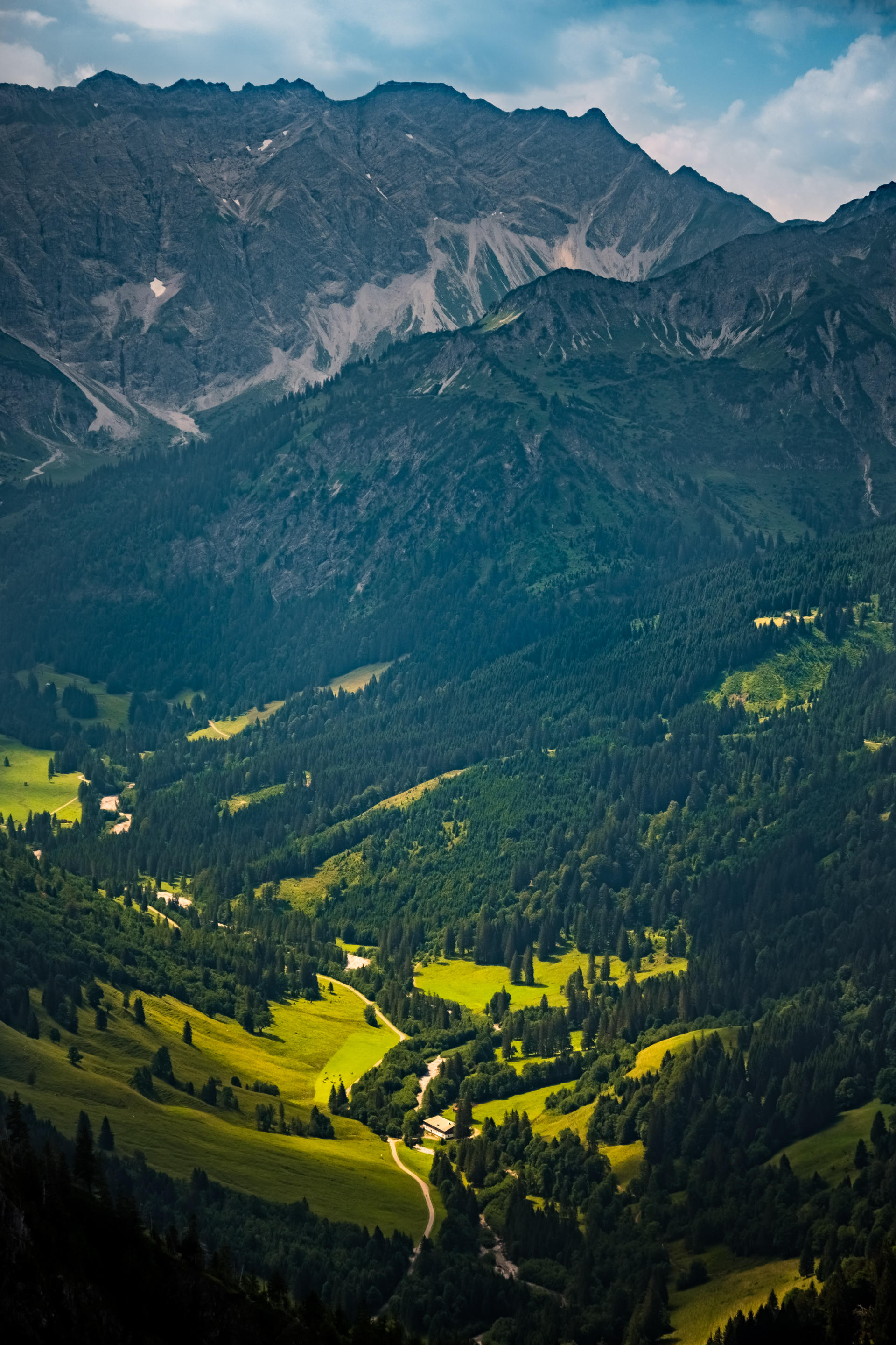 Mountains with lush green valleys and a winding road, under partly cloudy sky.