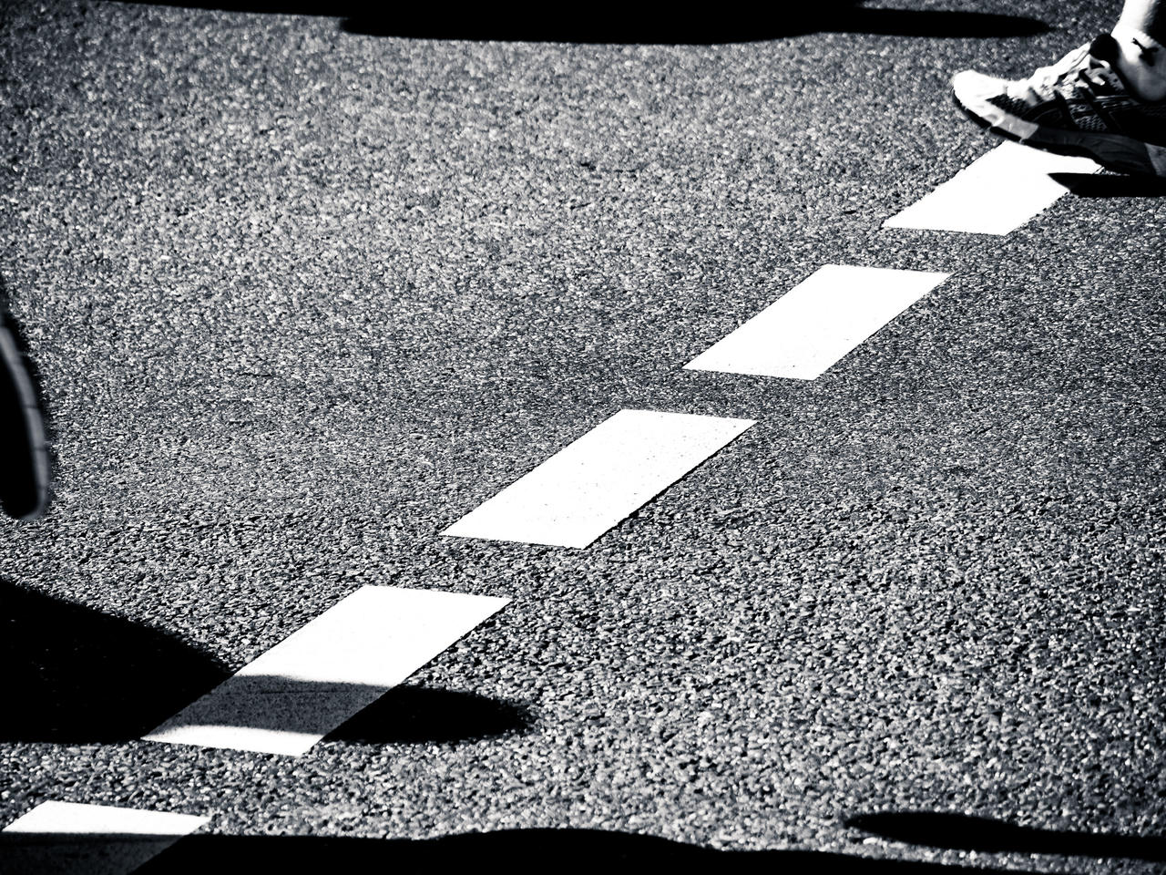 A pair of feet crossing a zebra crossing on a street.