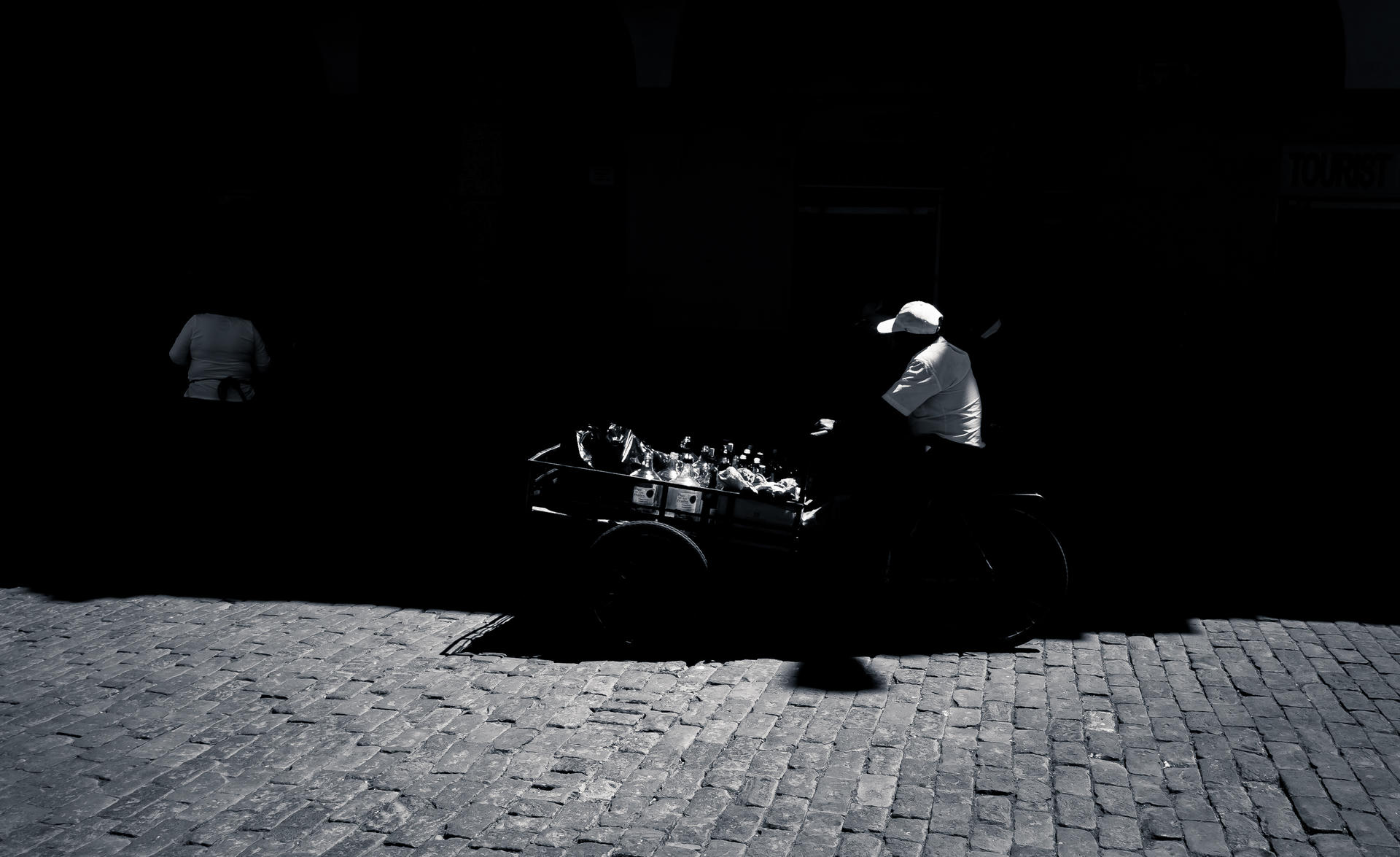 Silhouette of man riding a decorated motorcycle at night on brick road, another figure walking in background.