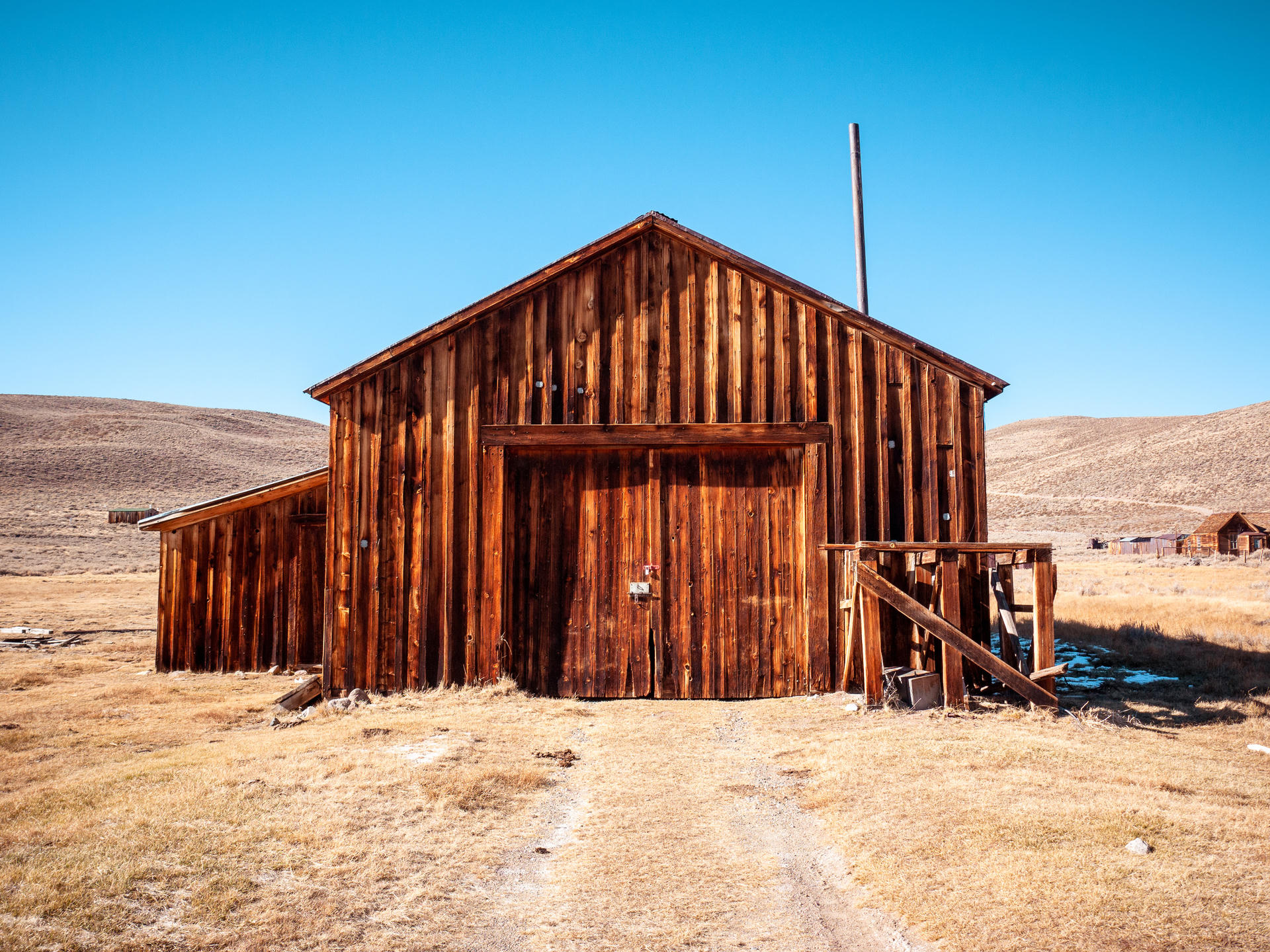 Weathered wooden barn with double doors, set in a dry, hilly landscape under clear blue sky.