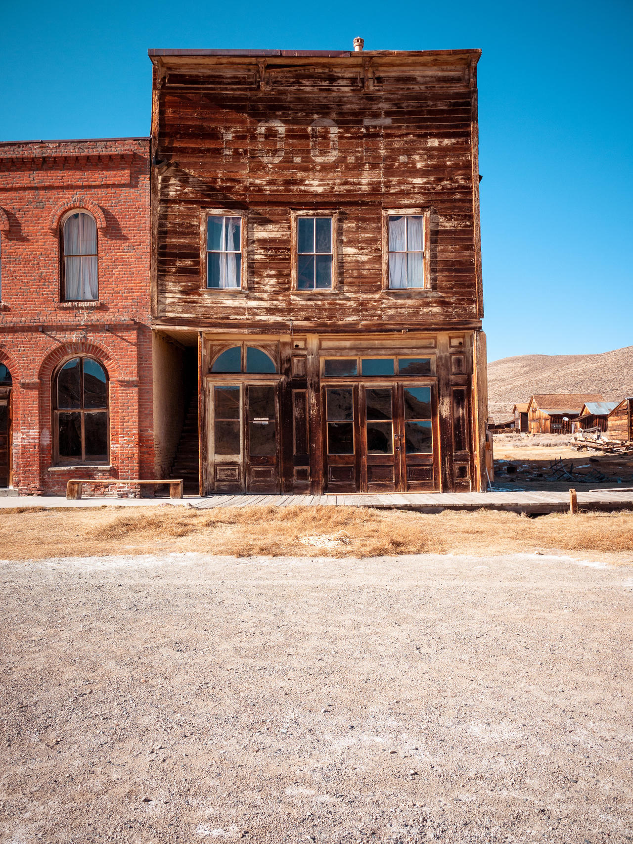 Weathered wooden building with peeling paint, arched windows, and central door, set in a desert-like town.