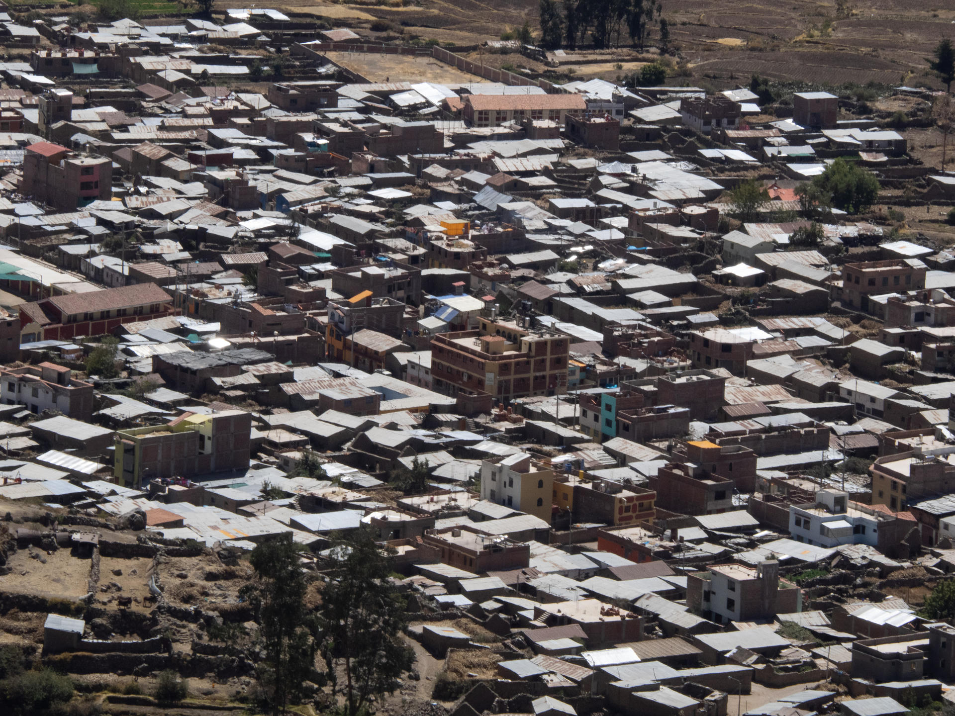 A densely packed slum area with numerous corrugated metal roofs, some buildings under construction, and sparse greenery.
