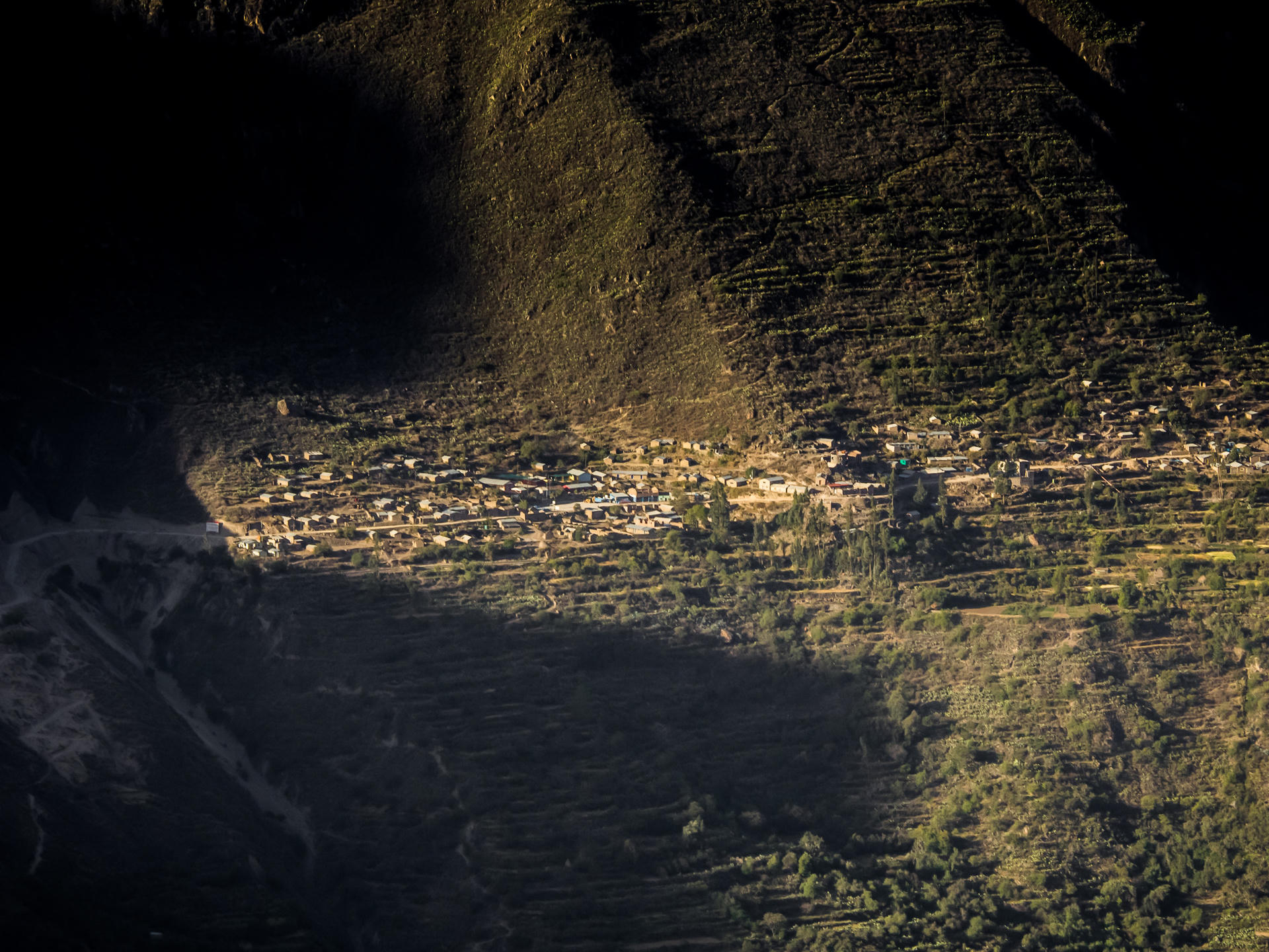 Aerial view of terraced fields at dusk, warm light on steps, dark silhouette of mountain in background.